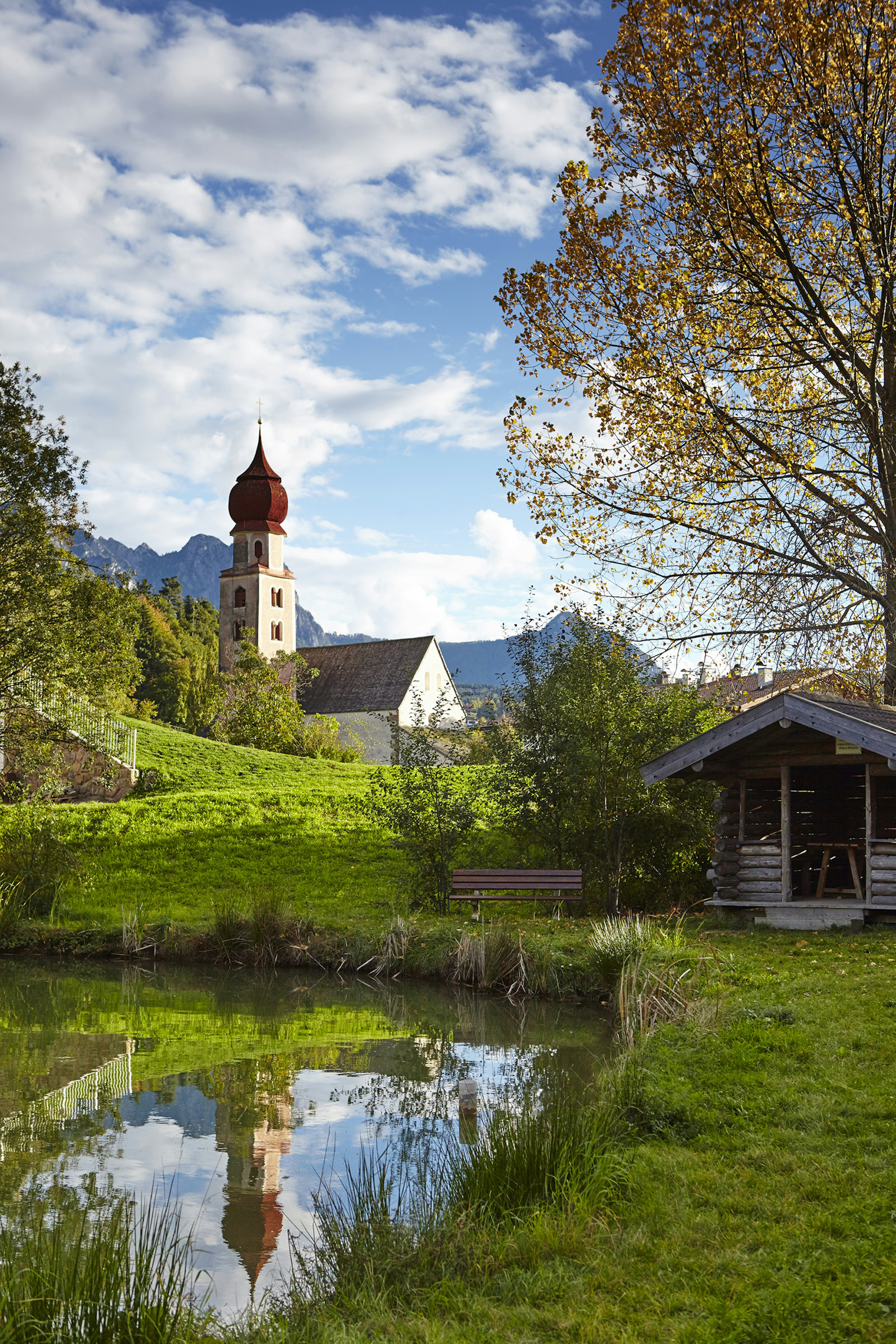 The red cupola of Sant'Osvaldo church is reflected in a mountain pond