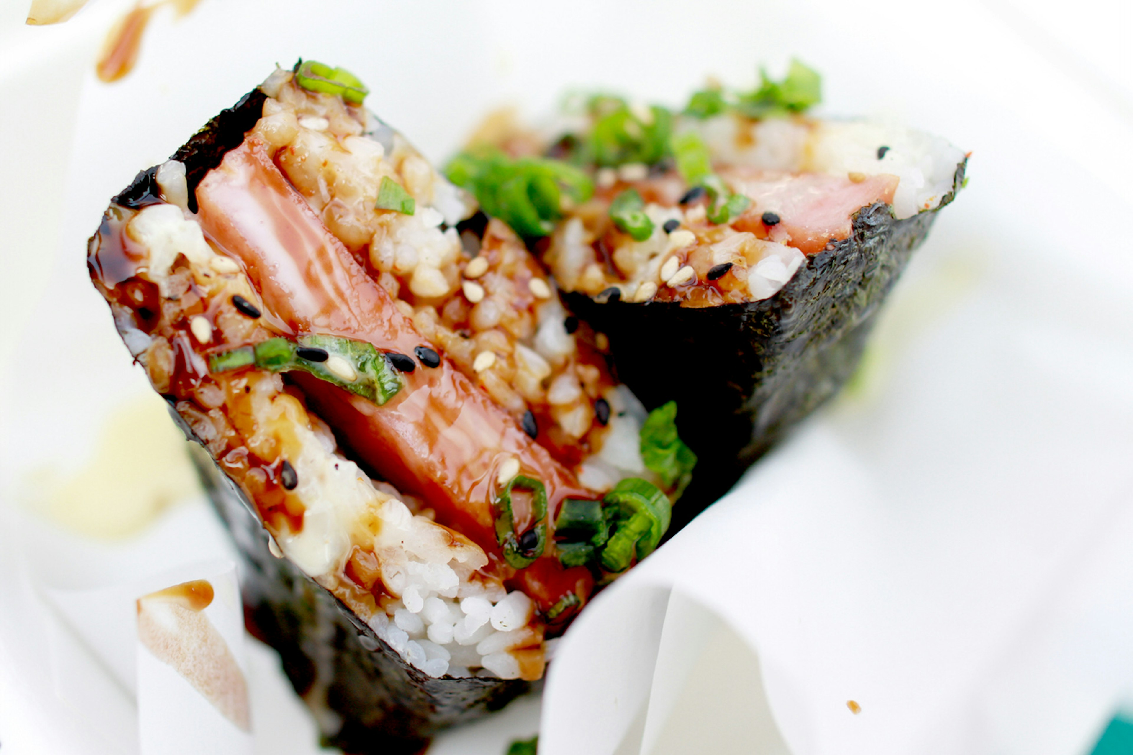 Closeup of a slice of grilled spam on top of a block of rice wrapped together with nori dried seaweed