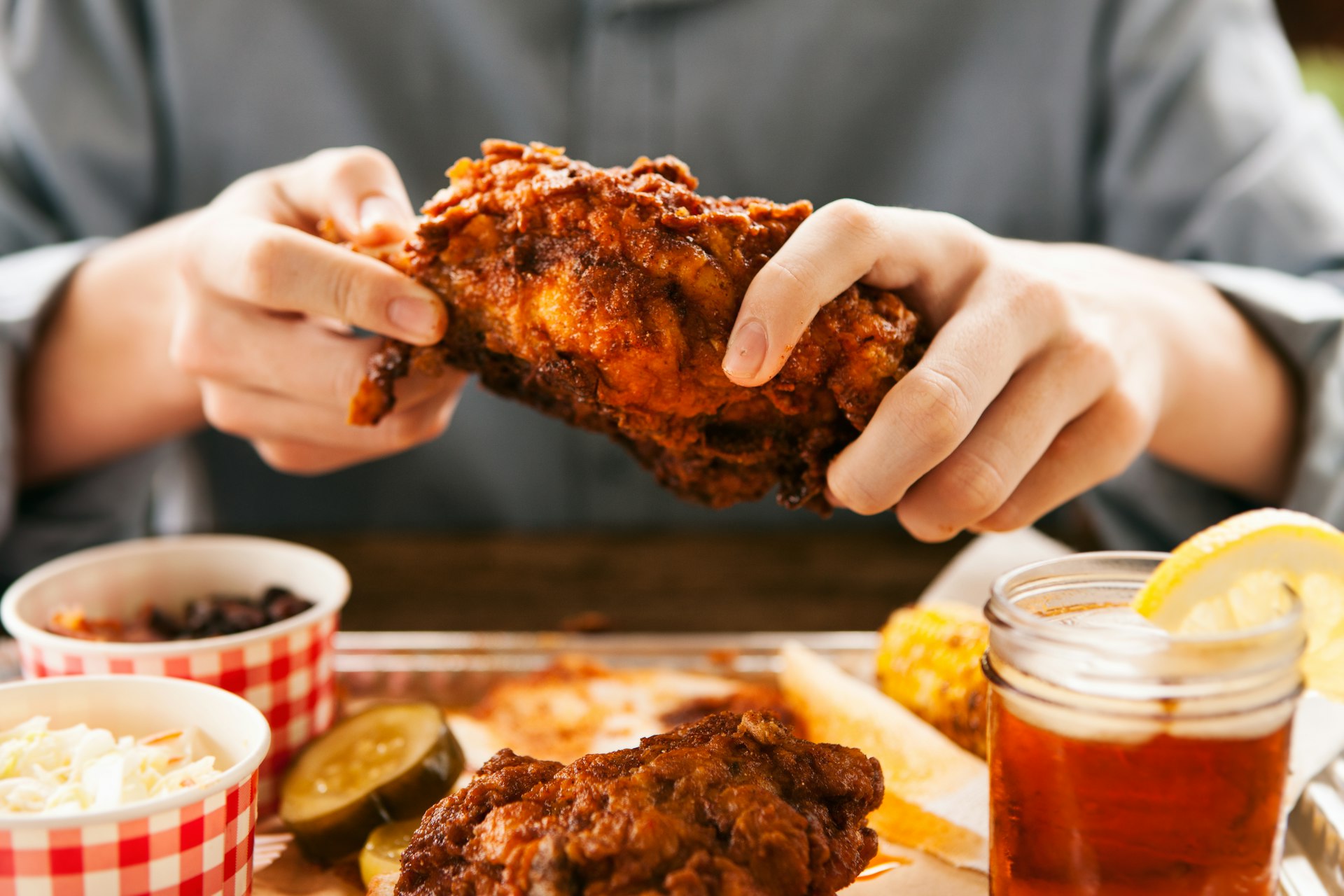 A person holds a hot chicken breast over a plate with red checker paper and two sides in bowls. Nashville.