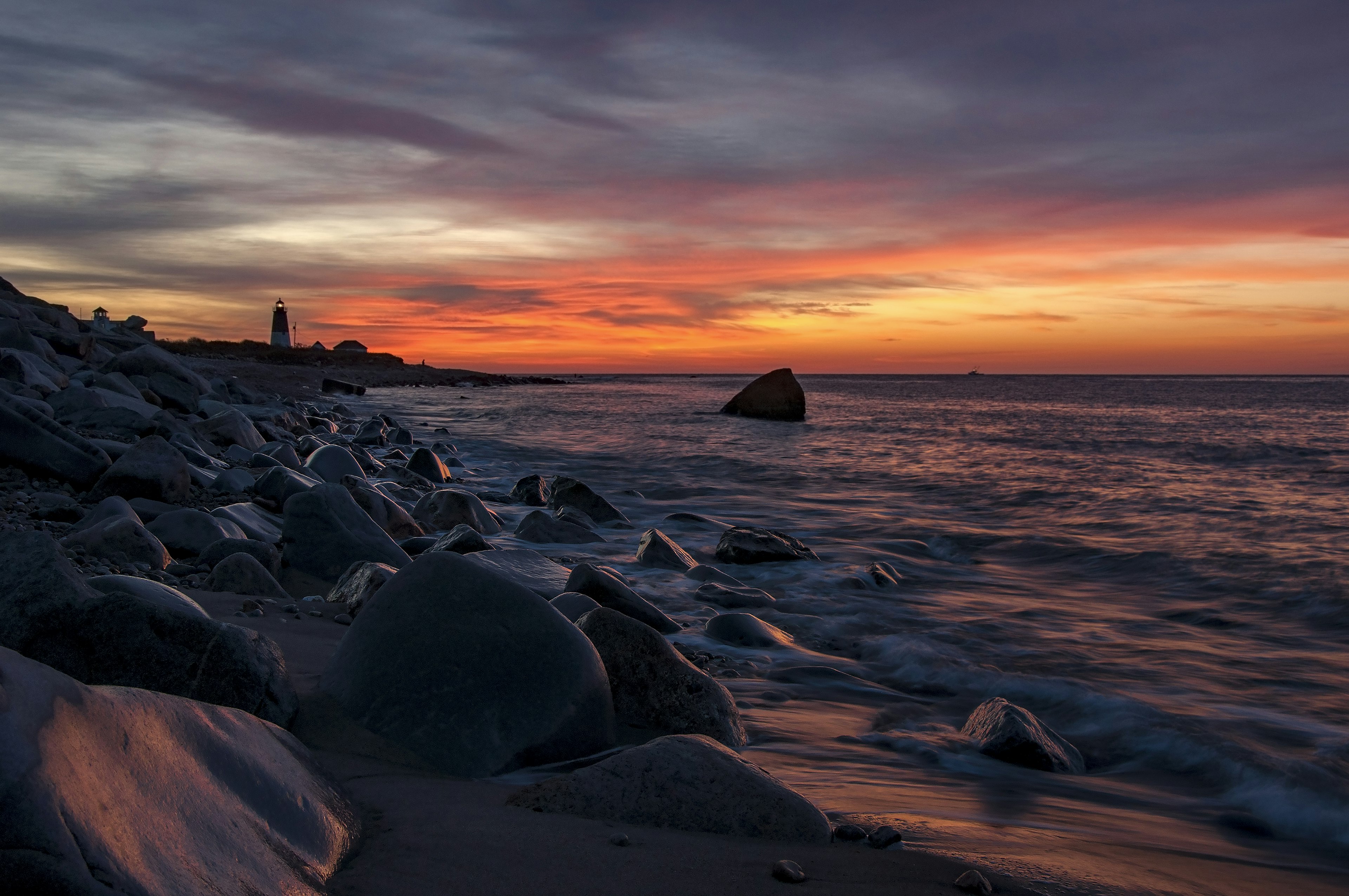 A pink and orange sunrise over a rocky shore with a lighthouse in the distance