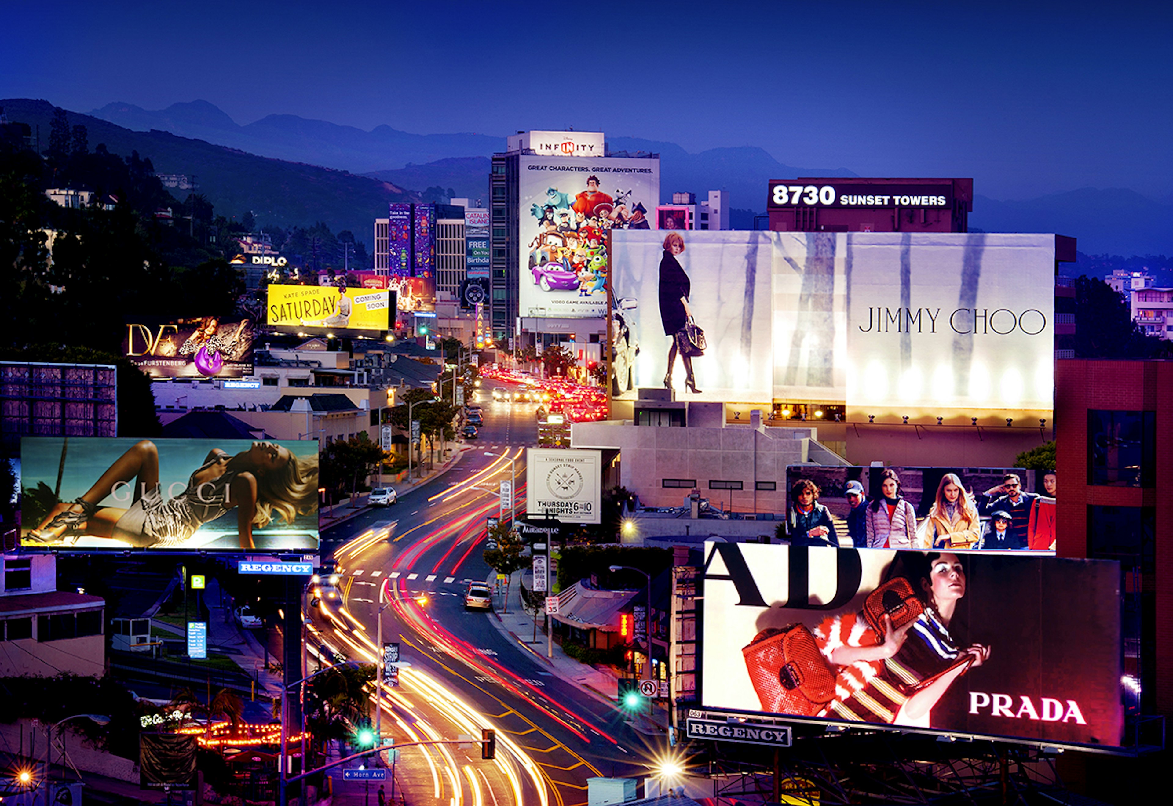 A series of large roof-top billboards flank the busy street of Sunset Blvd in the evening