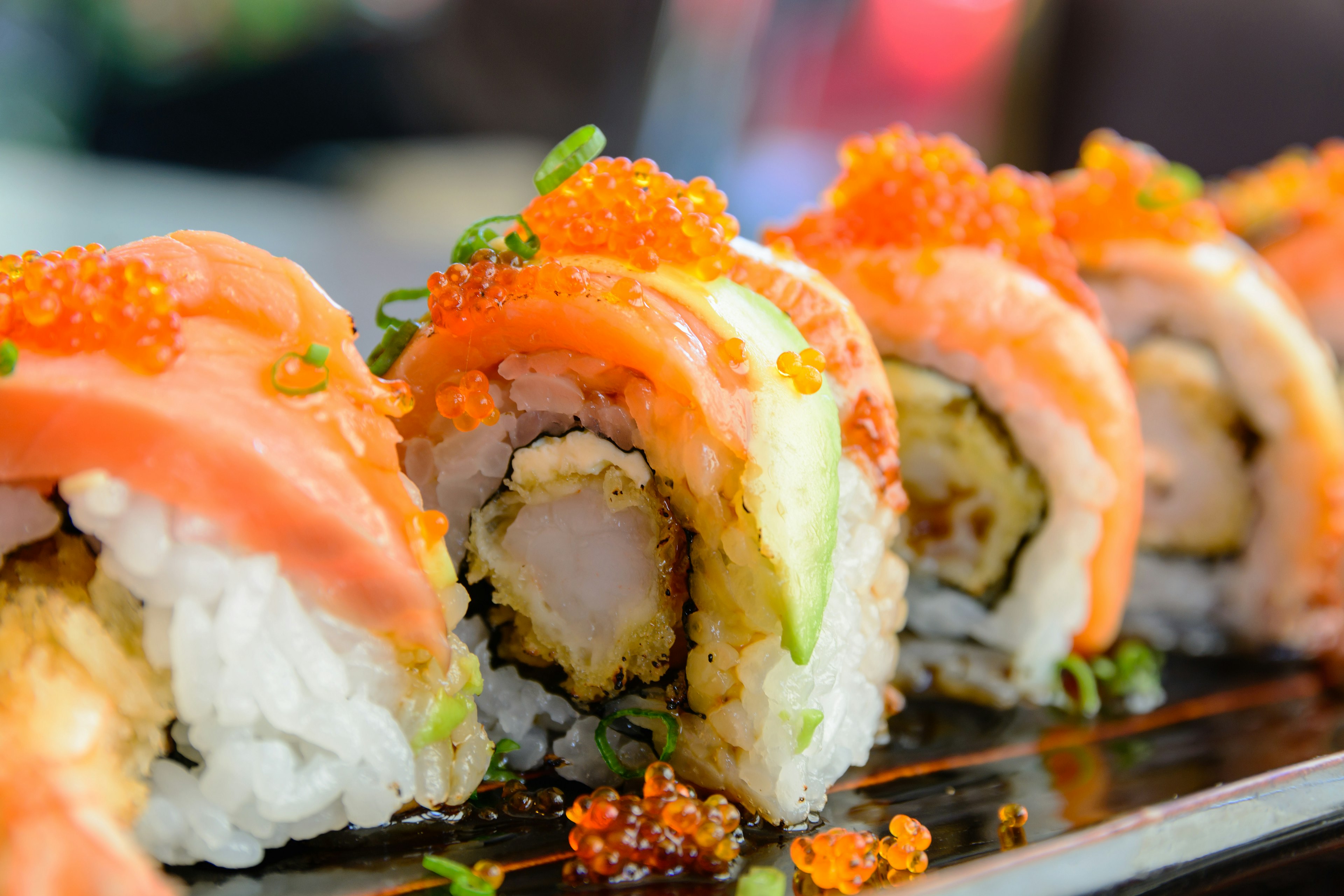 A close-up shot of sushi roll with salmon and shrimp tempura. The food is sat on a metallic plate.