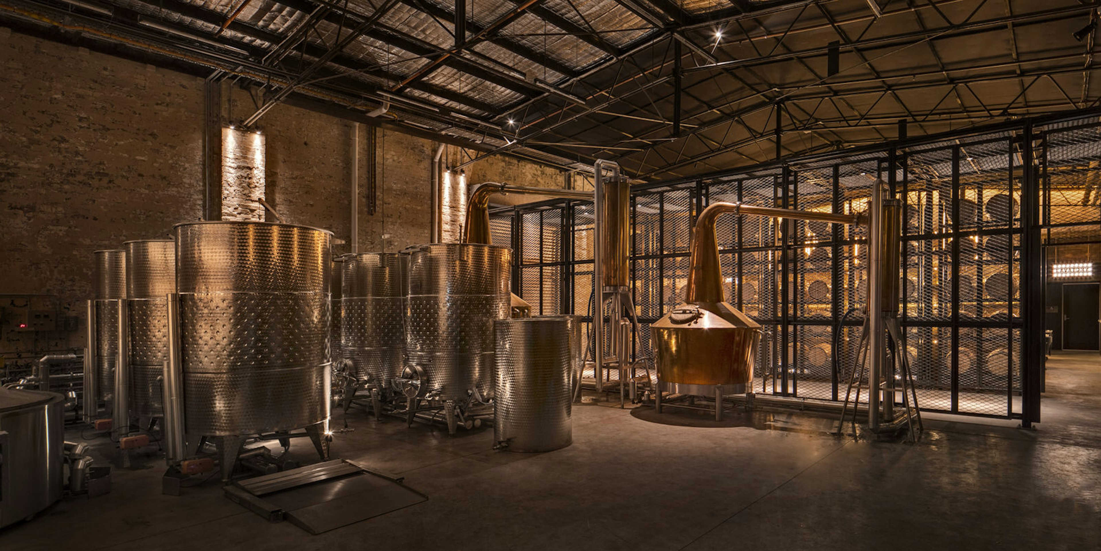 The warmly lit interior of Archie Rose distillery, Sydney, showing a small copper still and large steel washbacks.