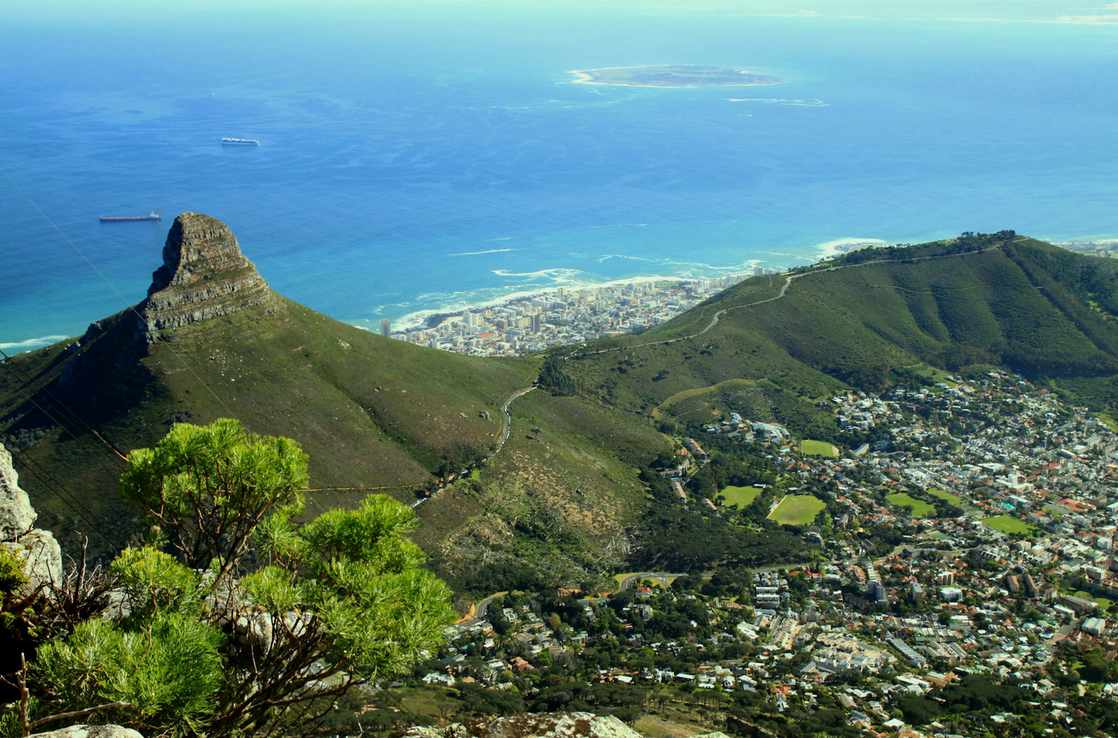 The green flanks of Lions Head rise to a pointy, rocky summit, with the blue ocean in the backdrop. The development of Cape Tow laps at the lower edges of Lions head and the ridge running from it © Renee Vititoe / 500px