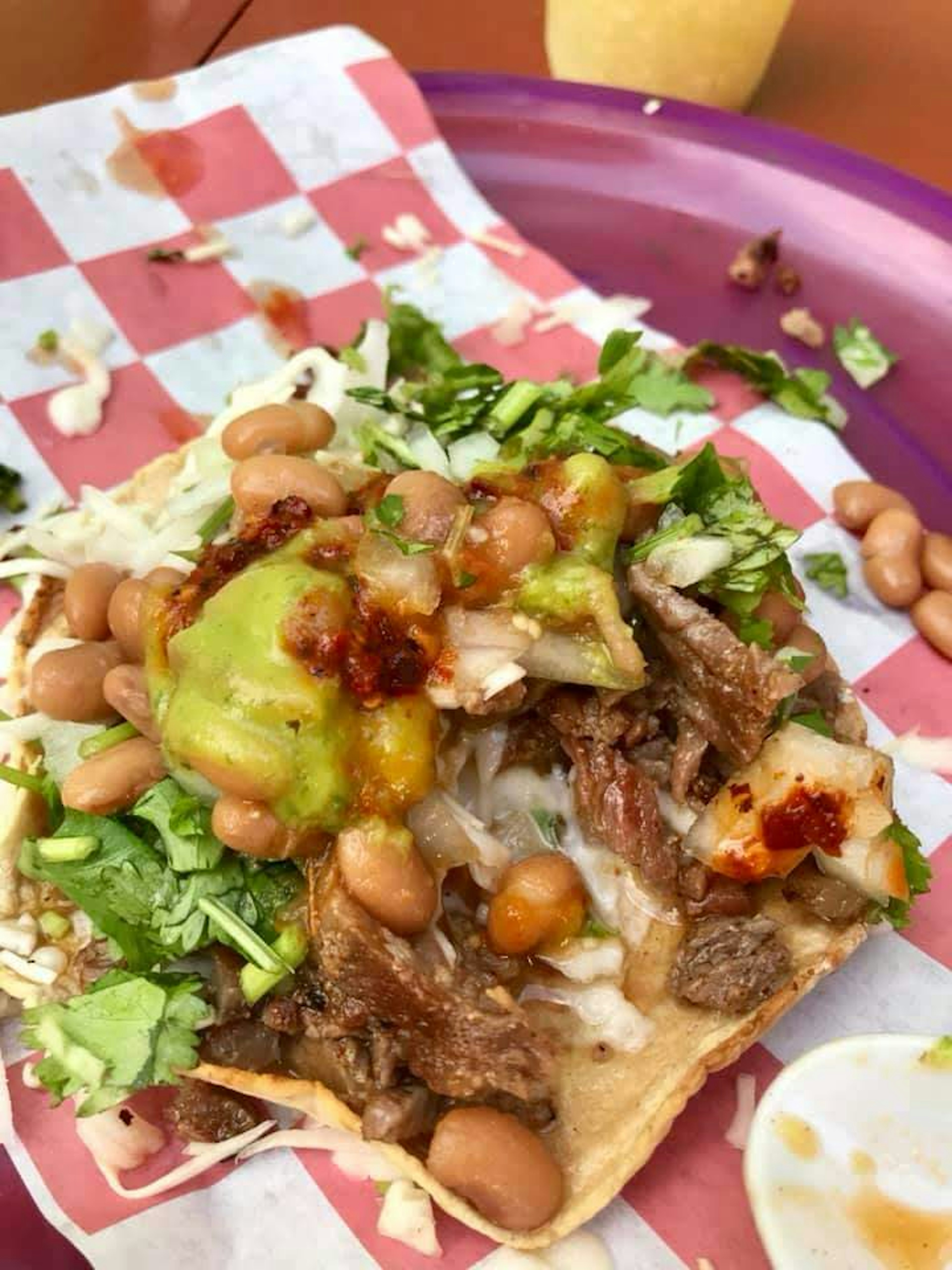 Closeup of an open soft taco piled with chopped meat, rice, beans, cilantro, onions and cheese on a red and white paper wrapper.