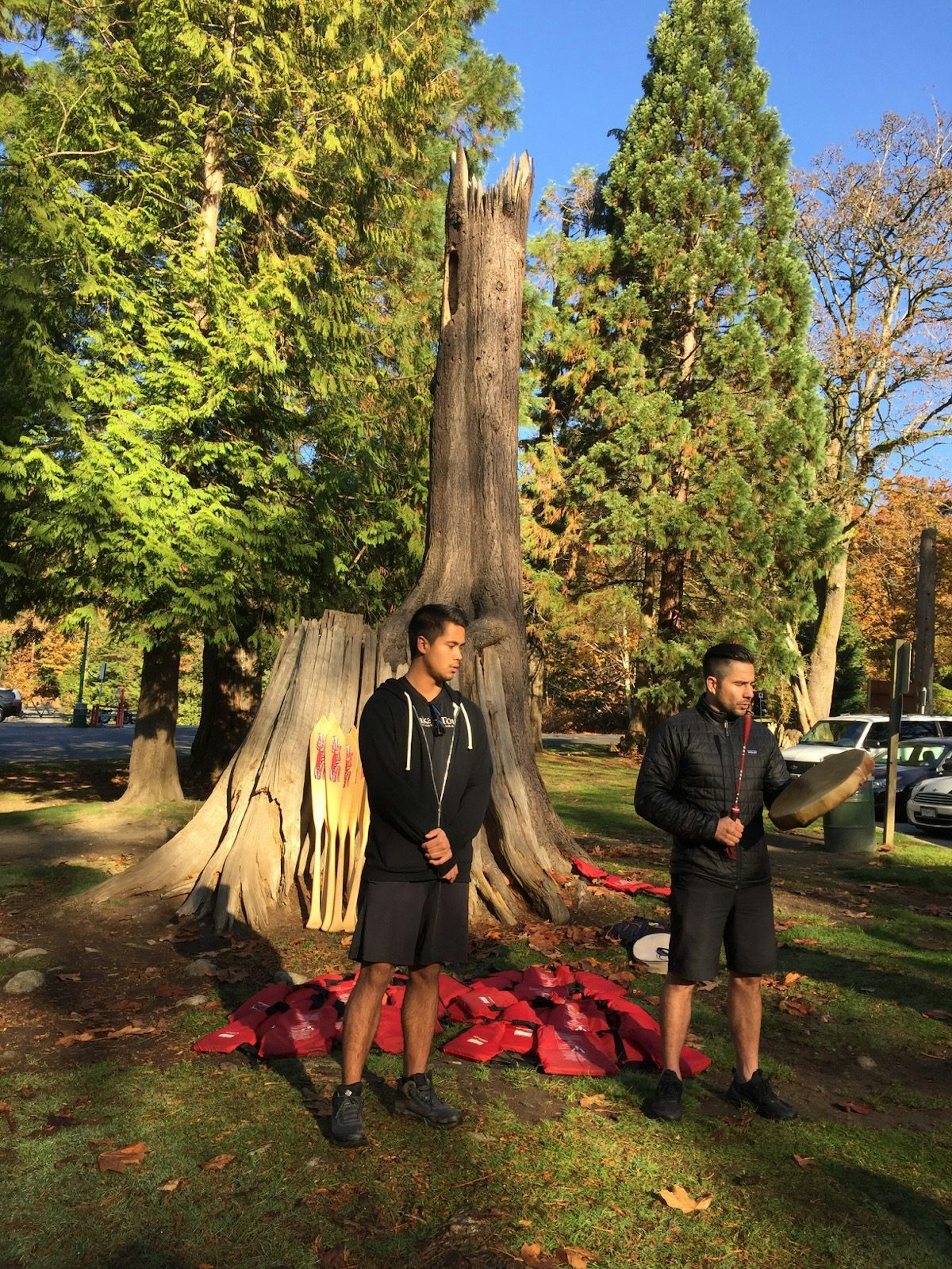 Surrounded by paddles and life jackets, a guide gives a traditional First Nations greeting using a drum