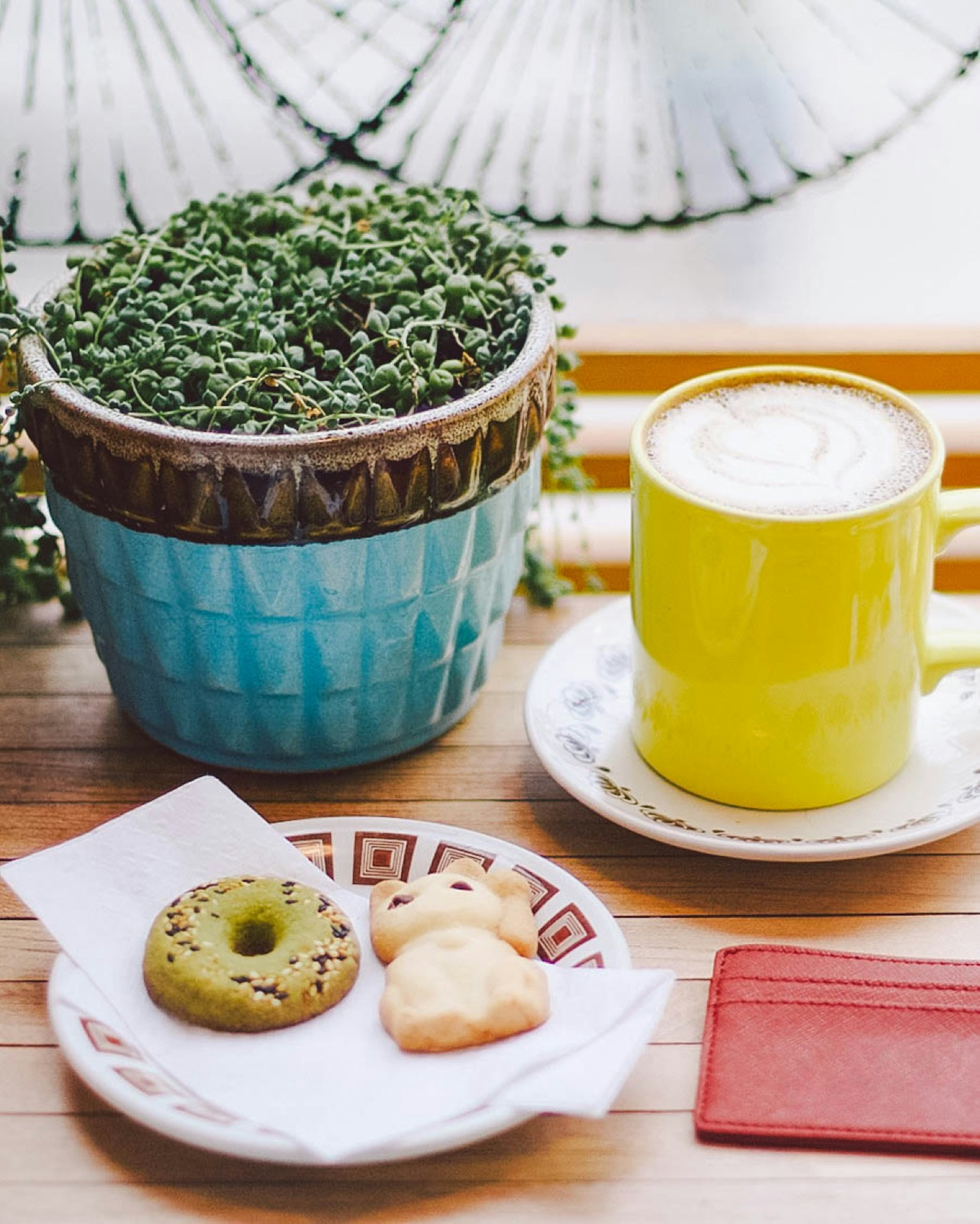 A yellow mug of coffee sits next to a potted plant and a small plate with two cookies on it © Jessica Lam / ϰϲʿ¼