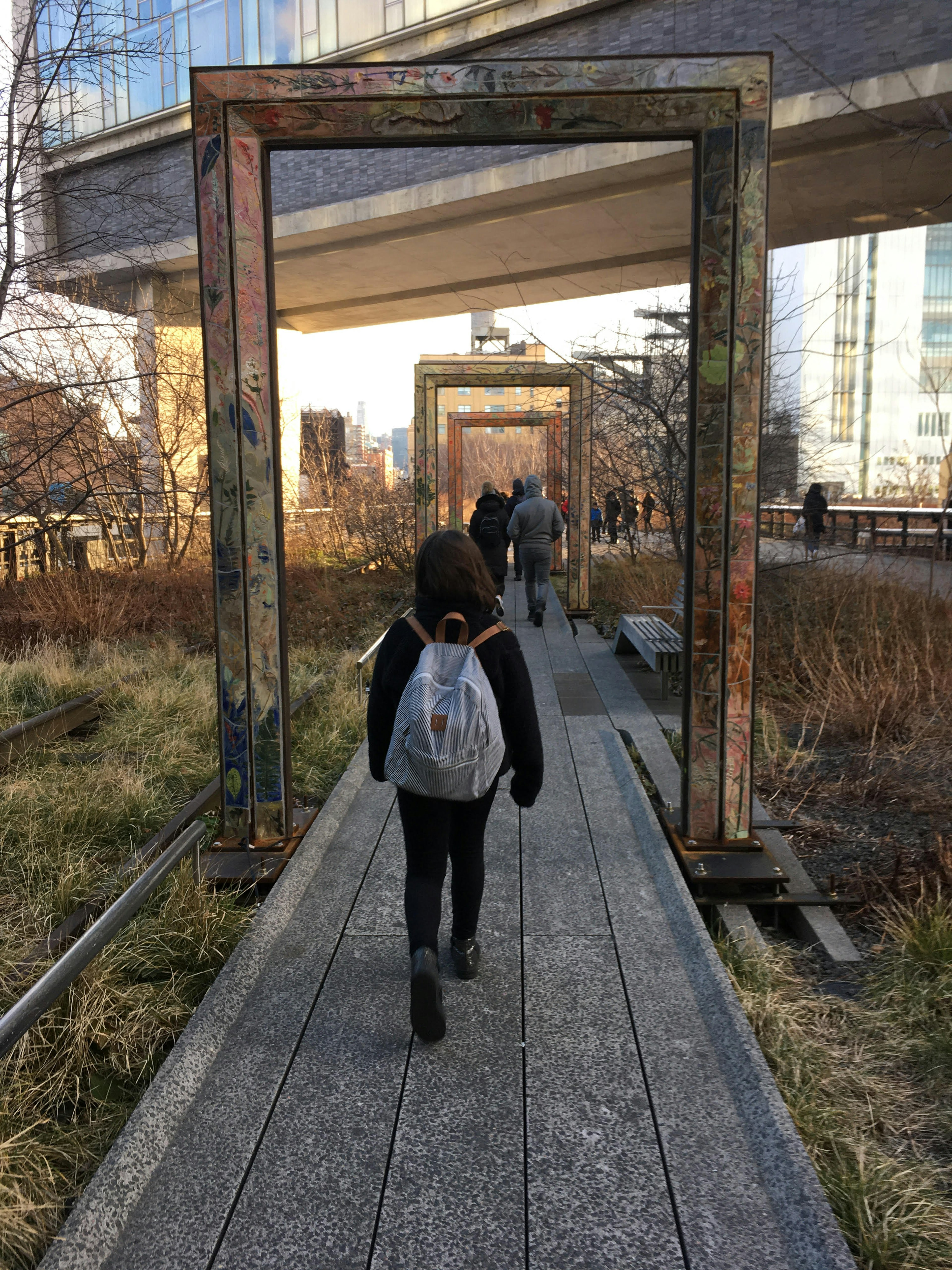 A girl wearing a hoodie is walking through a door frame that is outside in a public park.