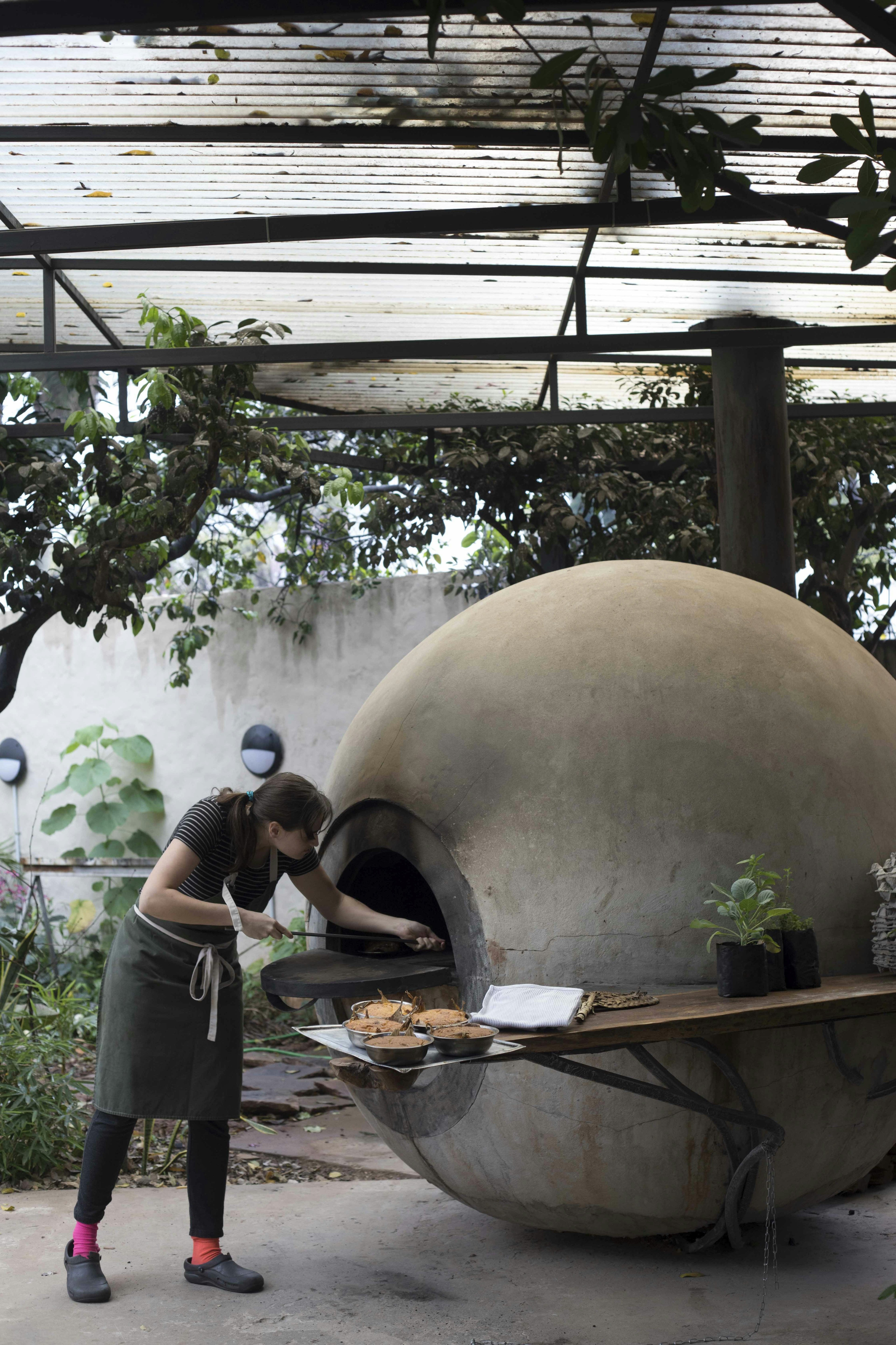 A woman pushes a tray into a large white stone oven in the shape of a sphere called a tatakua outside the Pakuri restaurant in Paraguay