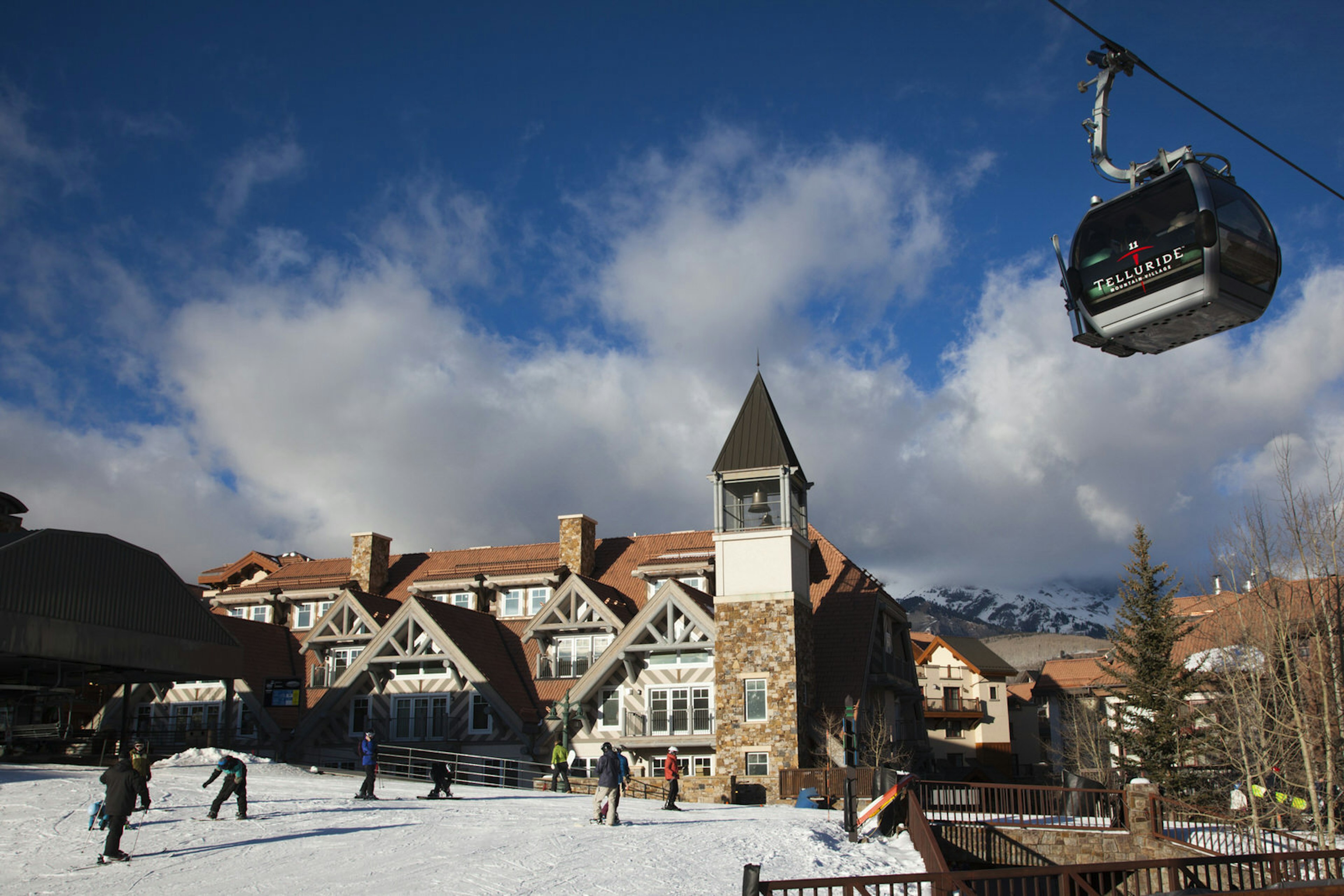 The Mountain Village Ski Area gondola passes overhead as people walk through the historic, snow covered town © Walter Bibikow / Getty Images