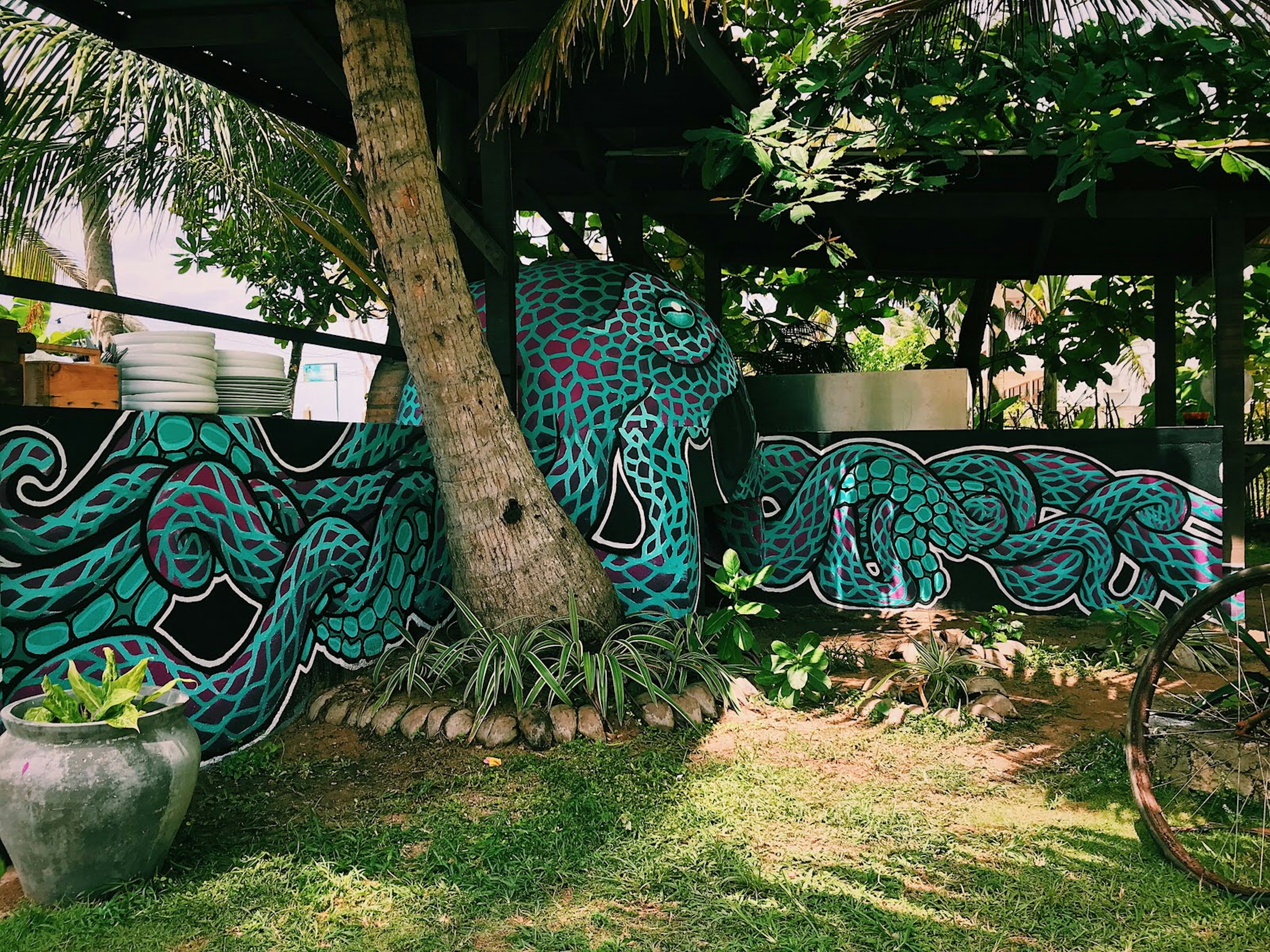 An outdoor pizza oven with a huge green and purple octopus painted on the dome. The octopus' tentacles stretch out onto walls next to the oven so it appears to wrap around the garden.