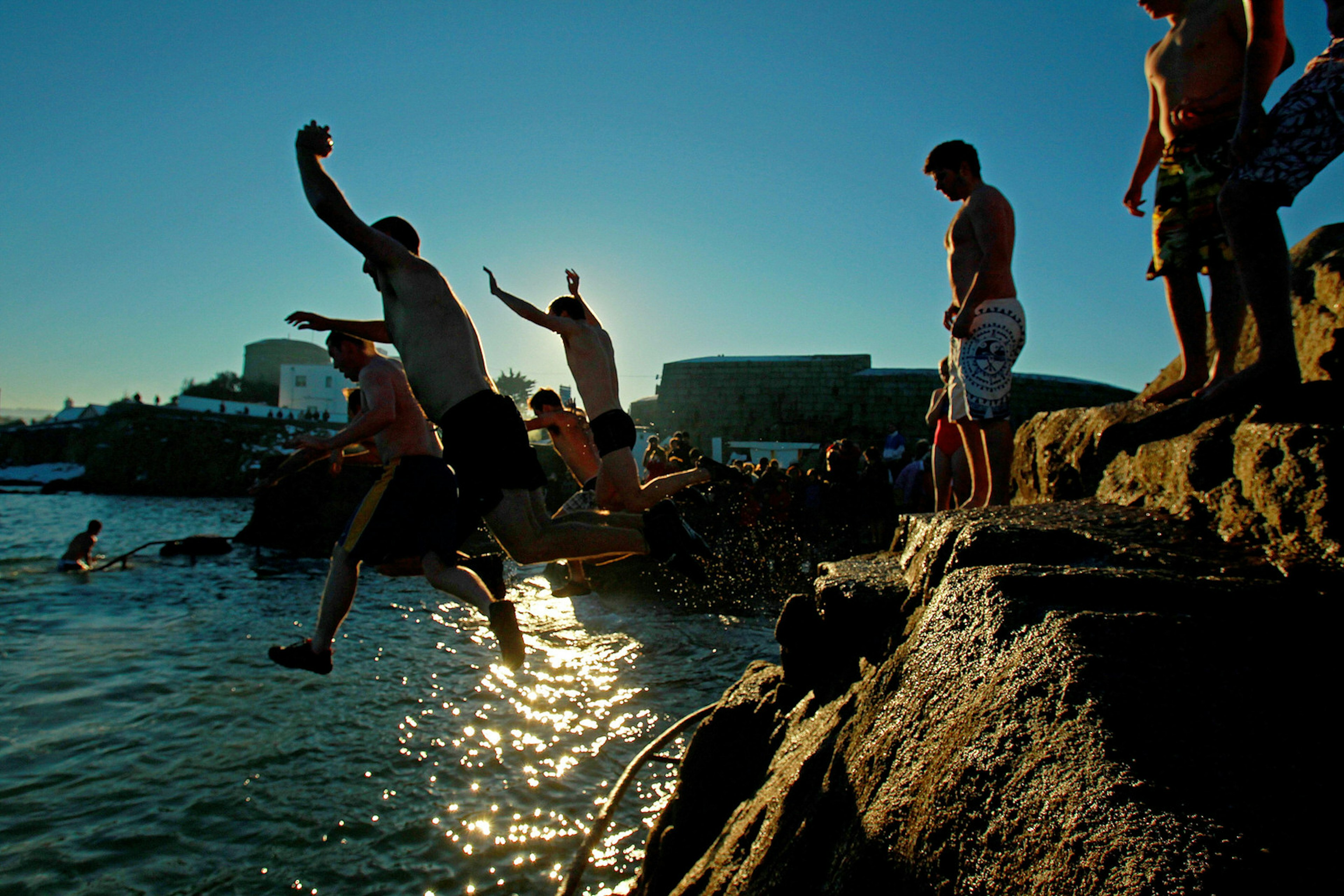 A group of people wearing bathing suits are jumping off the forty foot on a sunny day.