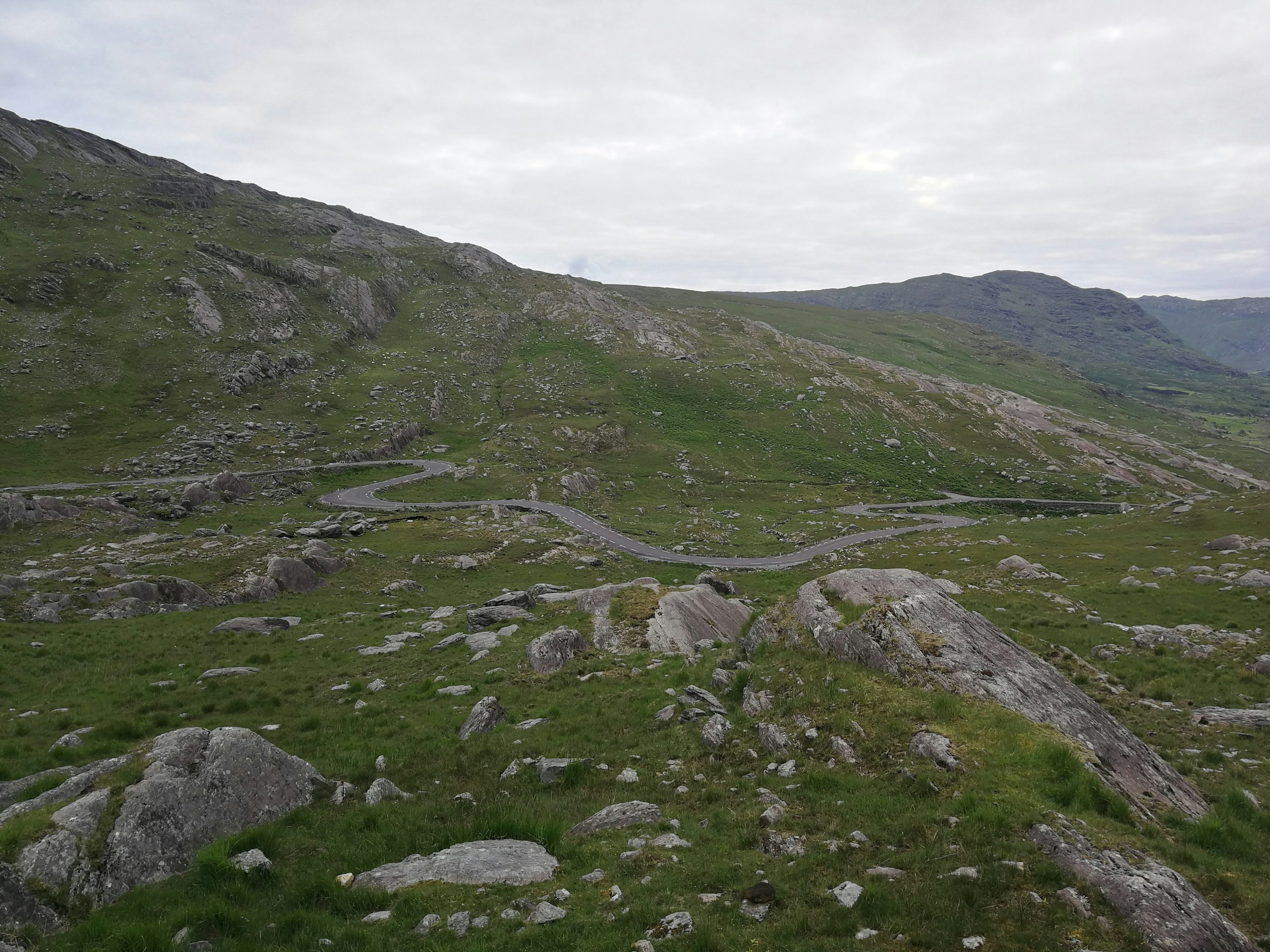 A narrow, winding road snakes over hilly landscape of grass and rocks.