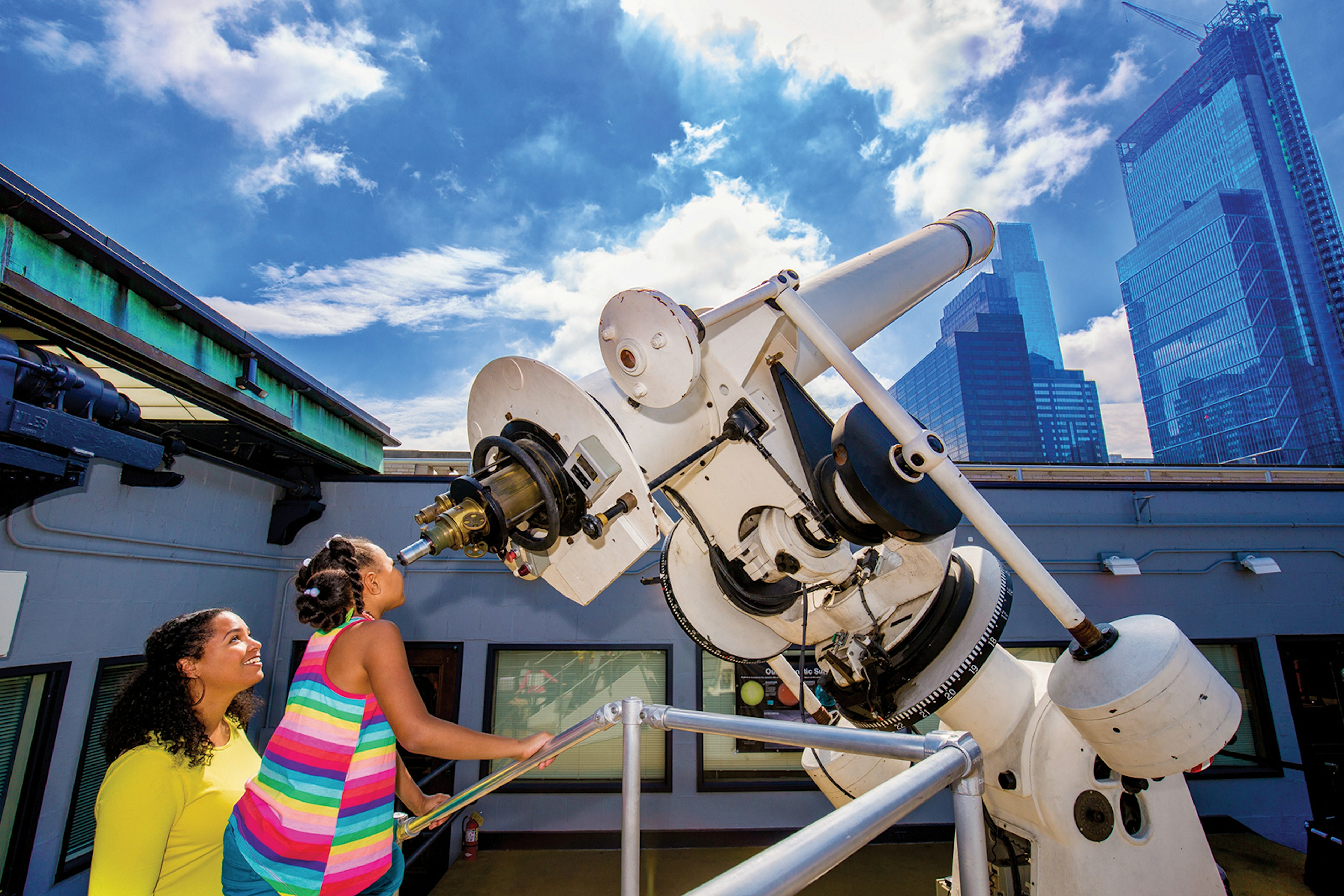 two children gaze into a telescope on a sunny day at the Franklin Museum J. Fusco for VISIT PHILADELPHIA®