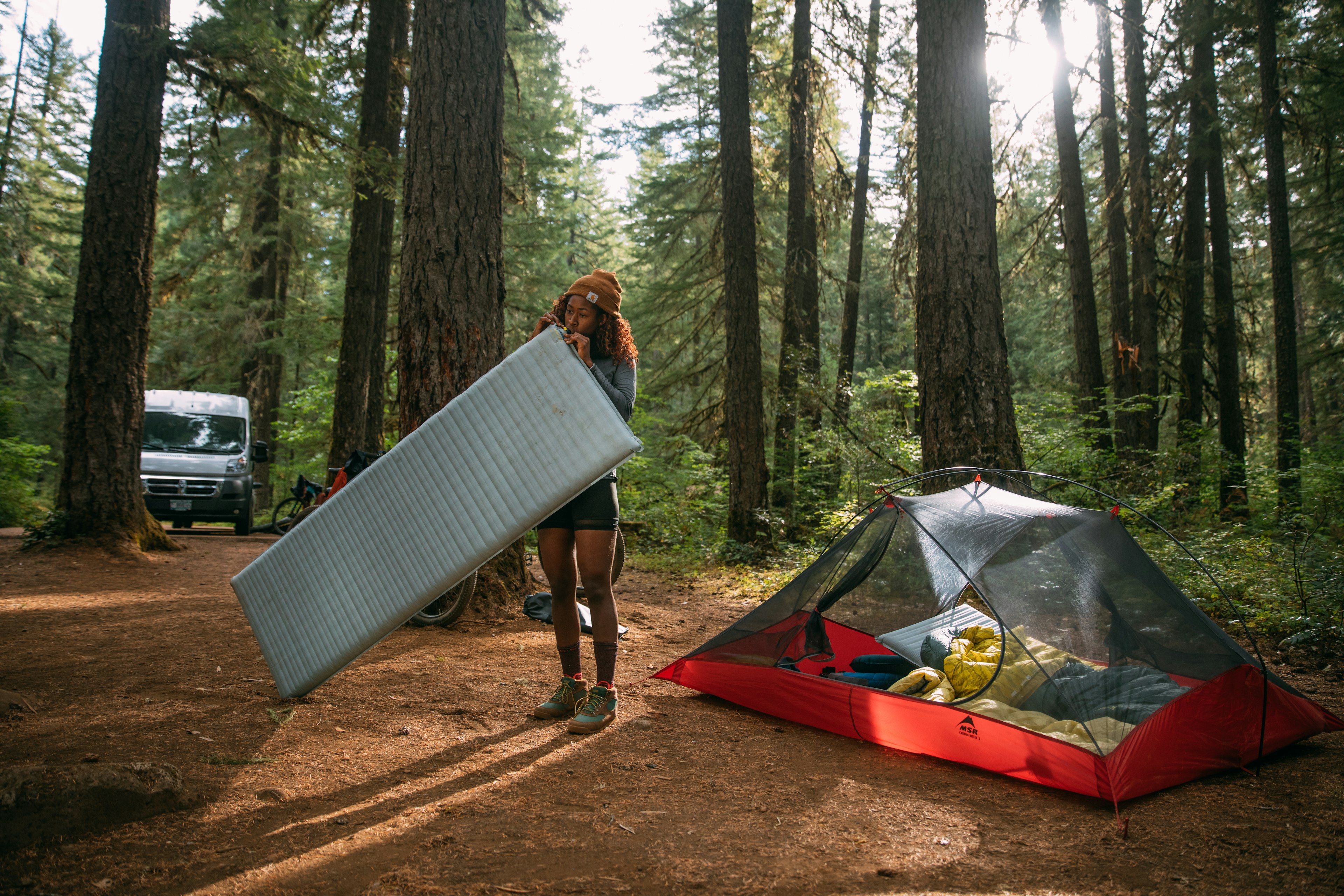 A woman inflates a sleeping bag in the woods