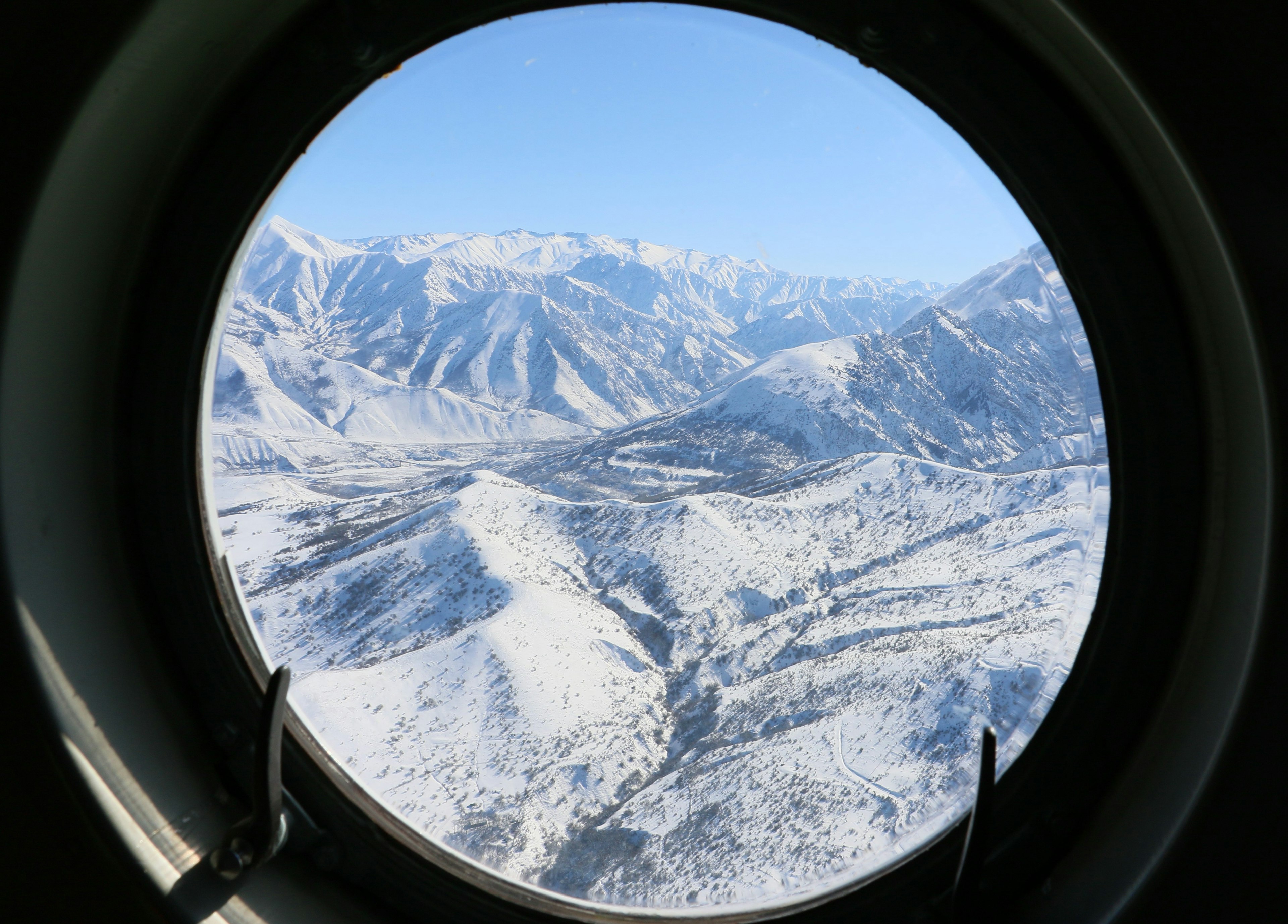 A view of beautiful white mountains through the circular window of a helicopter.