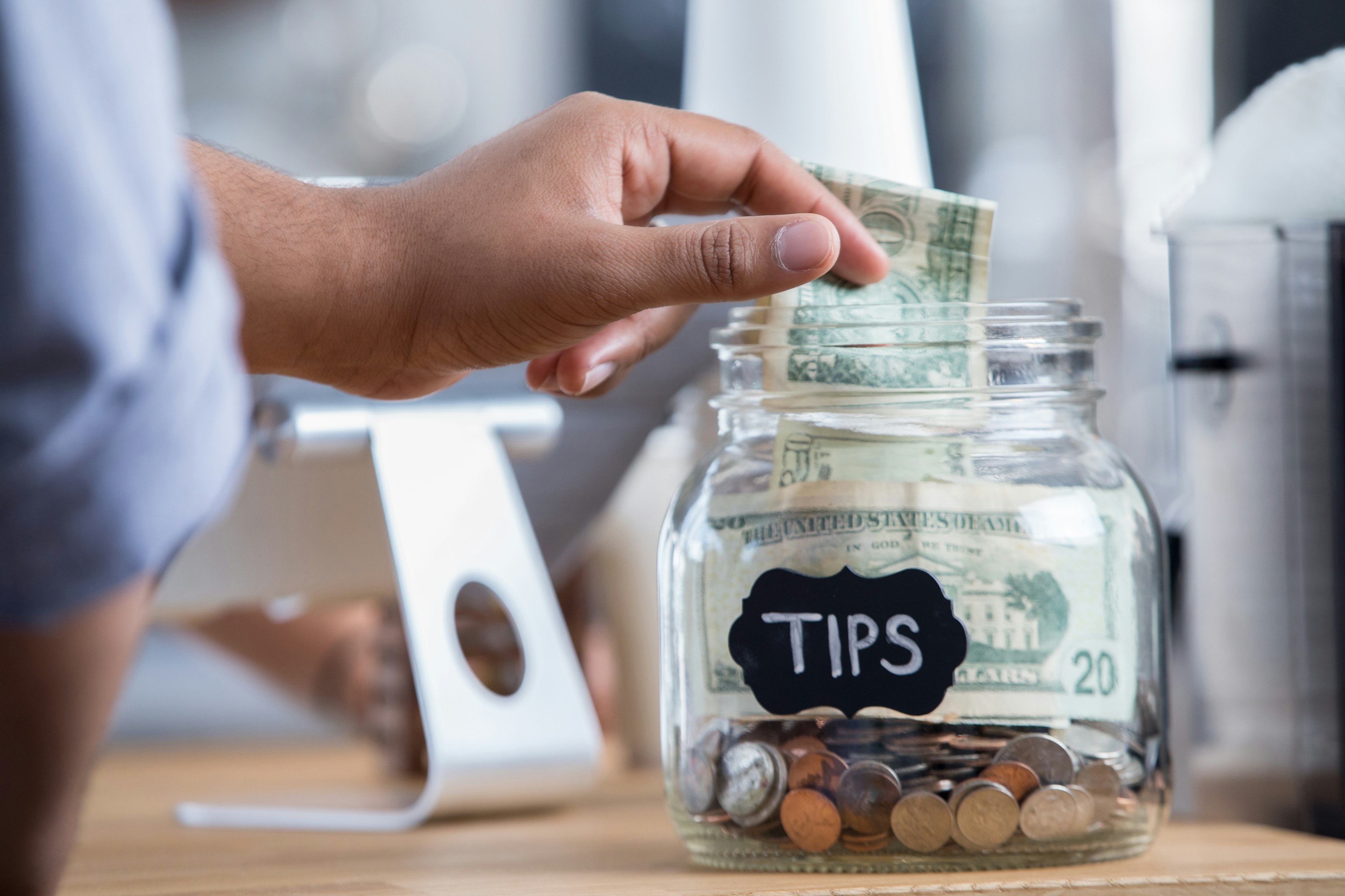 Coffee shop customer places cash in a tip jar