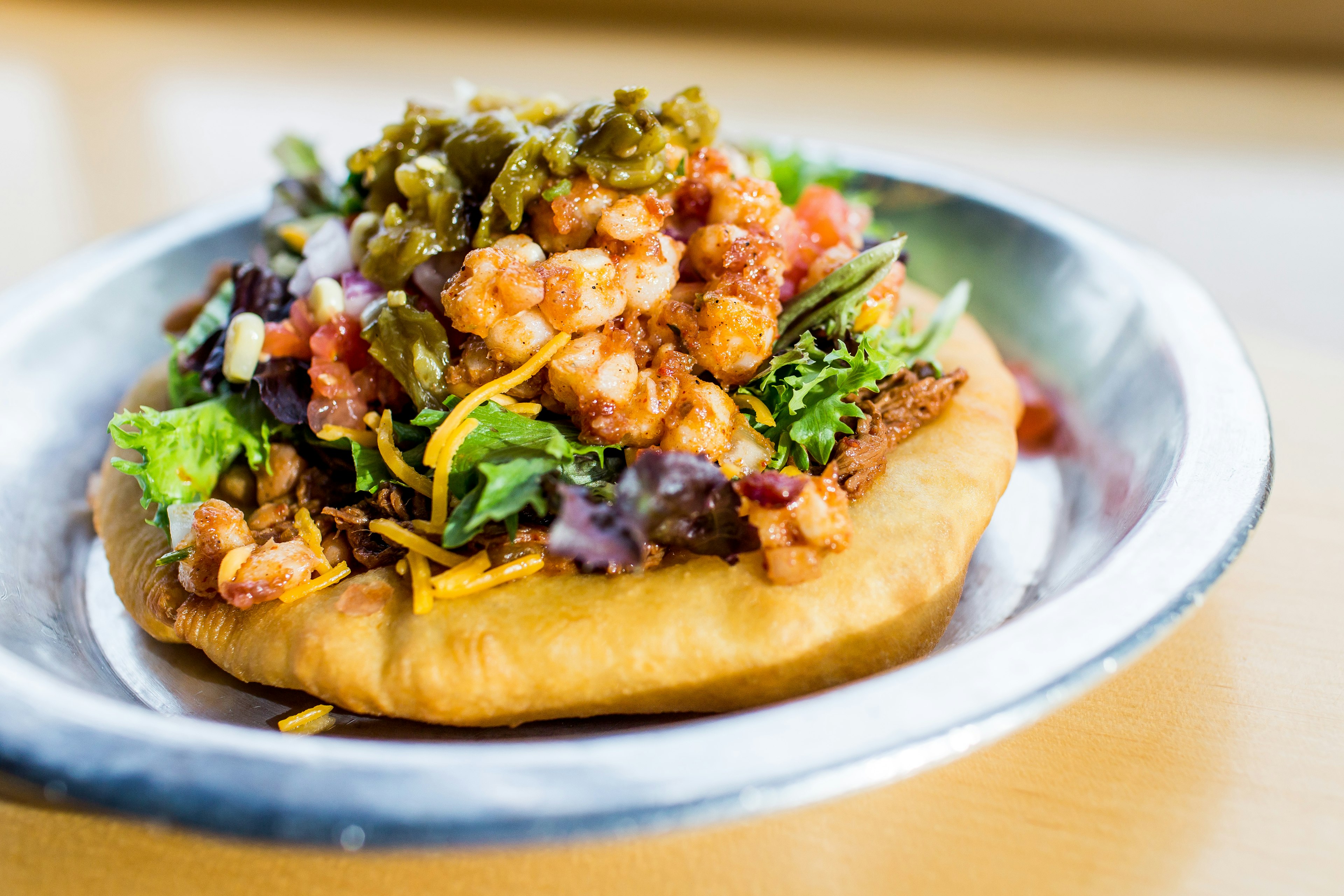 Closeup of a open-faced taco piled high with shredded meat, cheese, lettuce, tomatoes, corn and jalapenos; Indigenous food