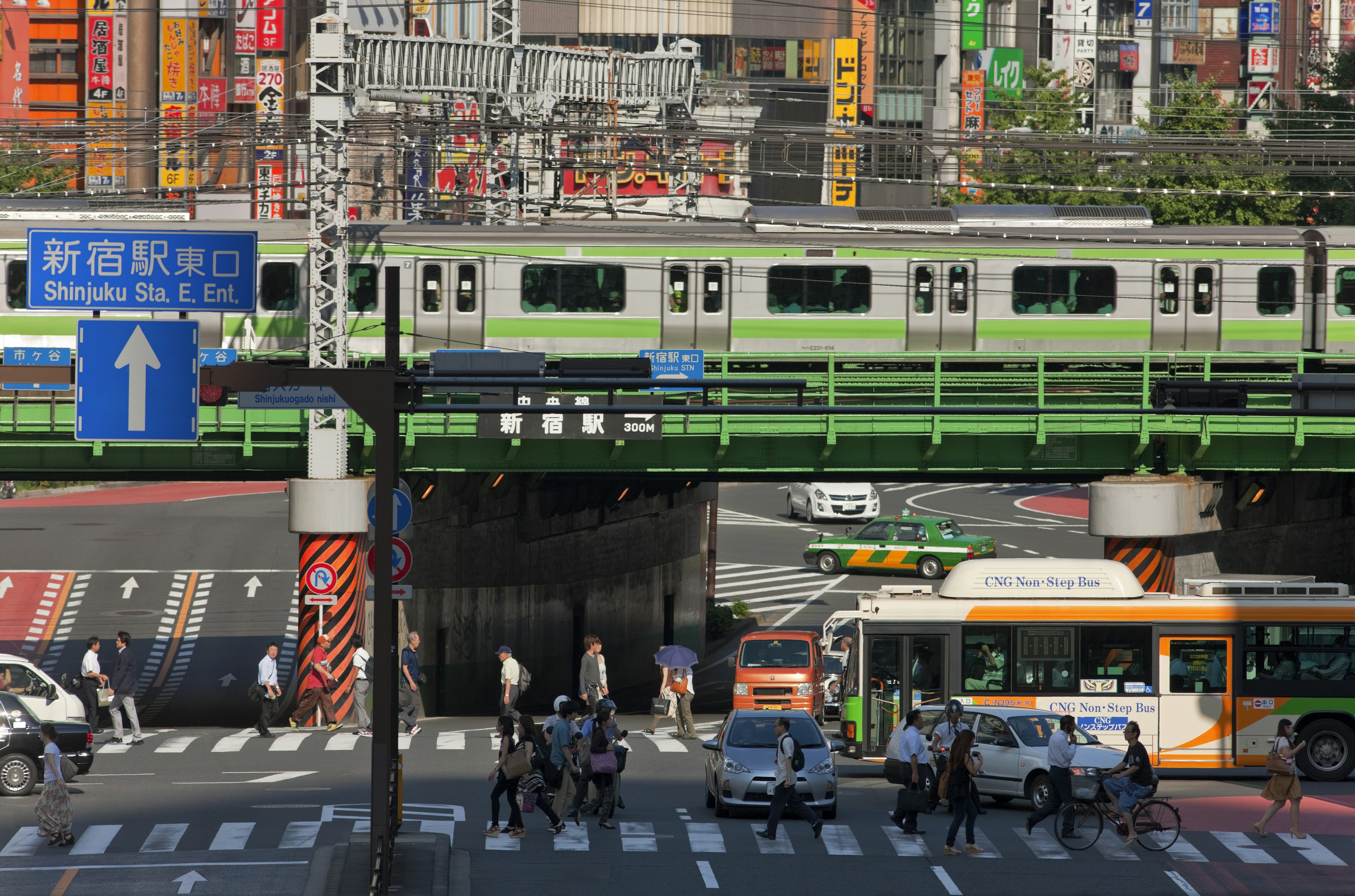 The Yamonte Line, in Tokyo Japan, on a sunny day. Cars and pedestrians passing by are in view.