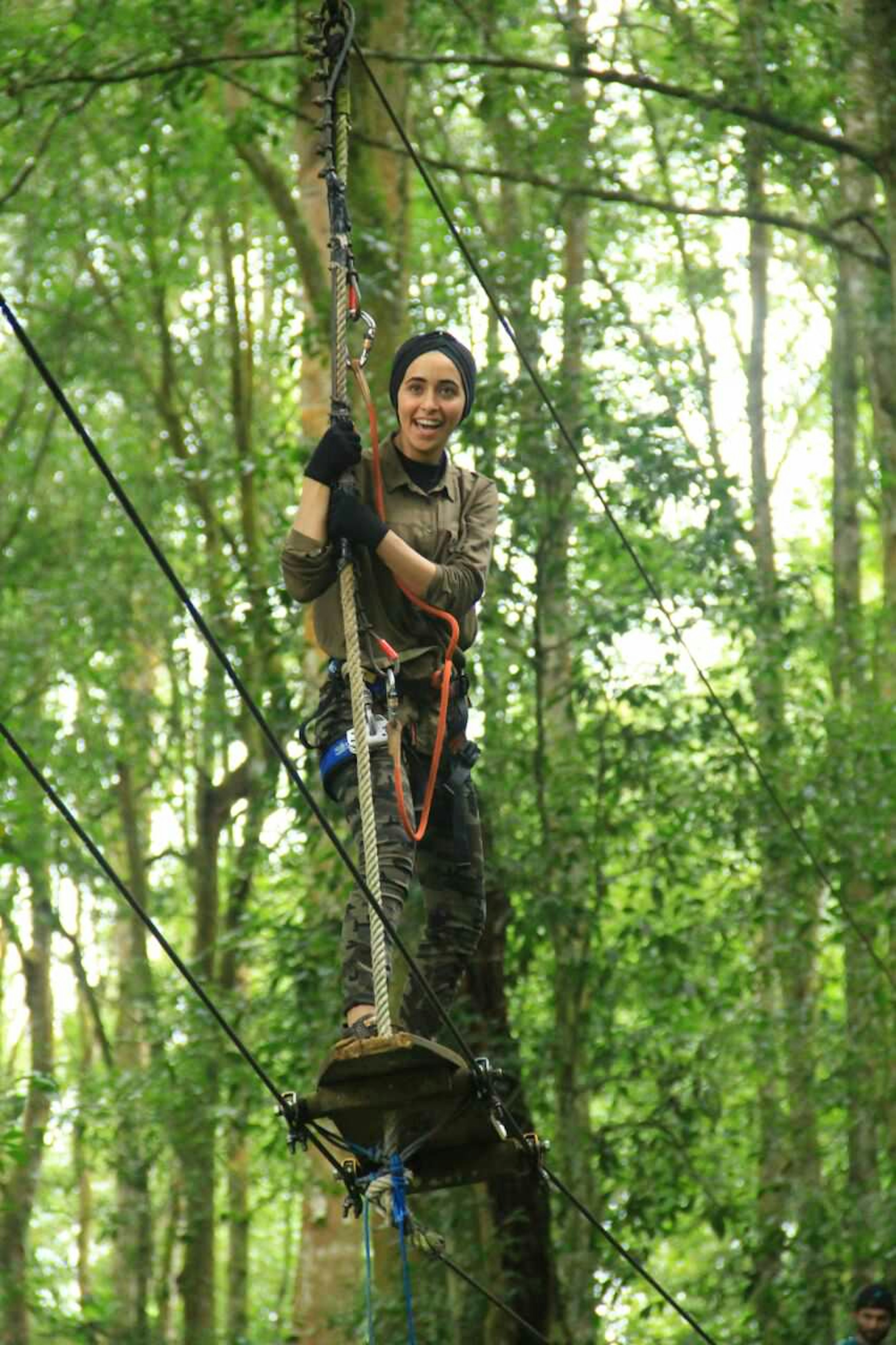 A woman works her way along a tightrope hung between trees in Bali. She is attached to the lines with a harness.