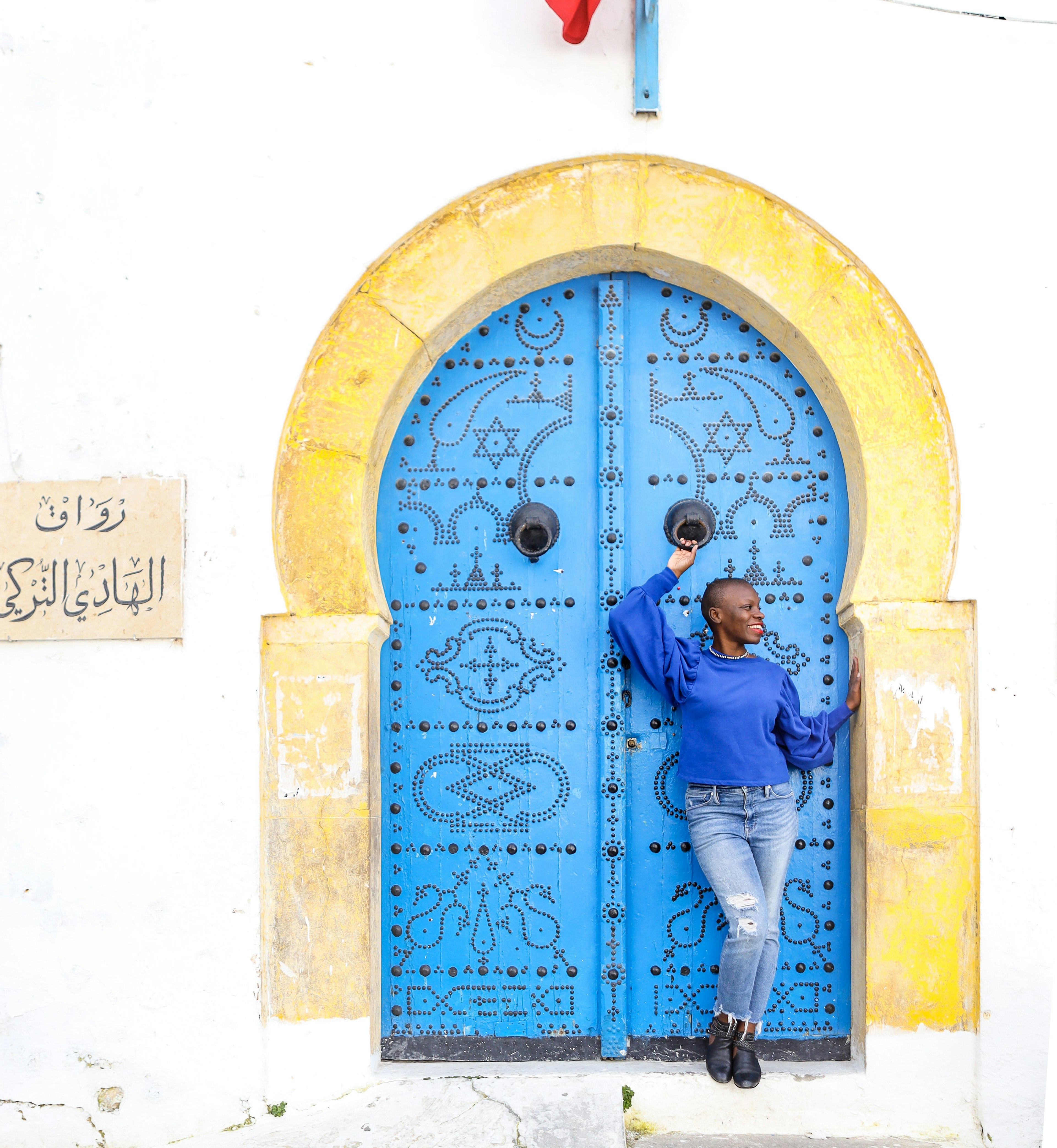 Jessica Nabongo stands in front of a large blue door with a yellow frame on her quest to travel to every country in the world