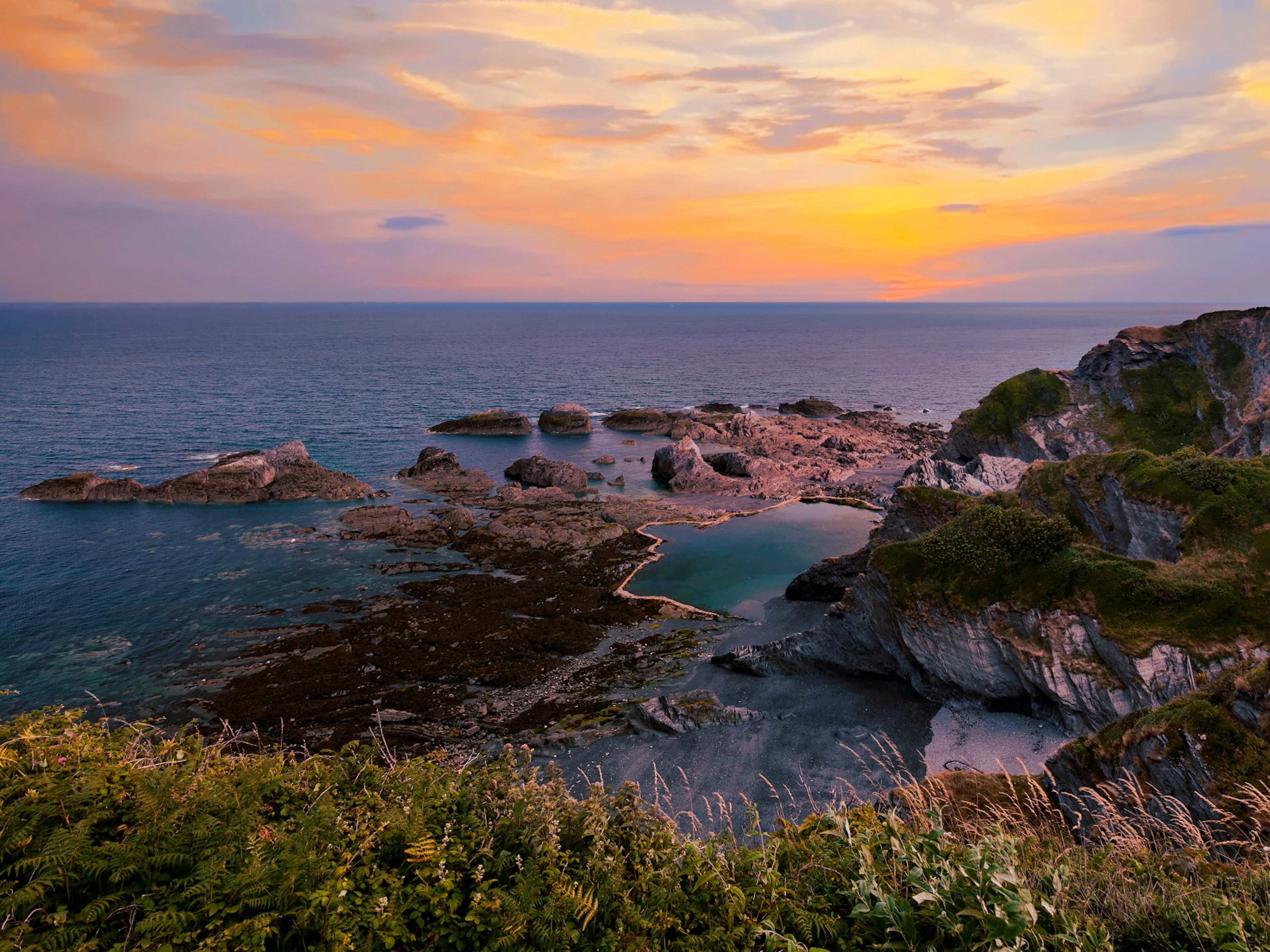 A sunset over the rocks pools of Tunnels Beach in Devon