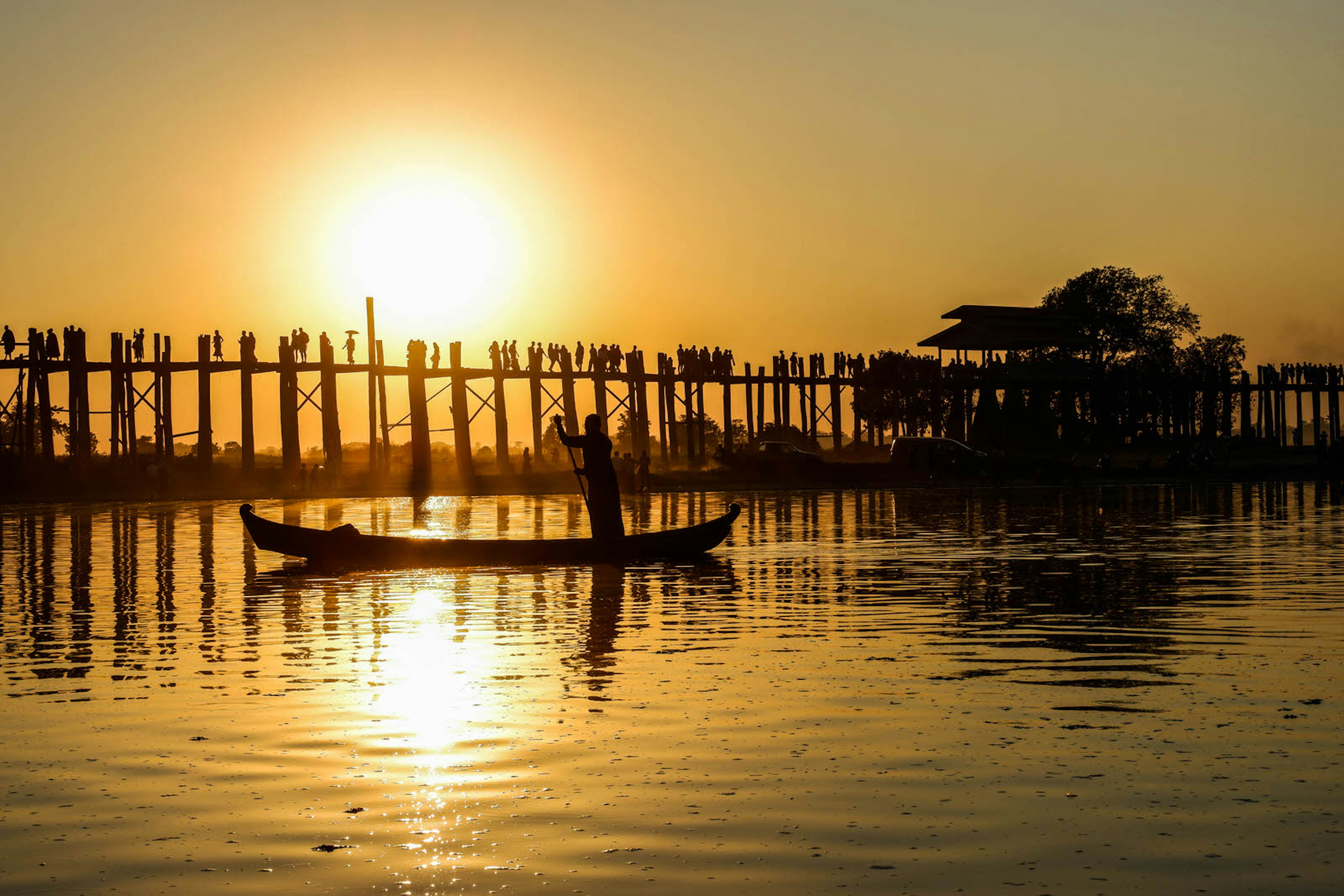 A boatman rows past U-Bein bridge at sunset