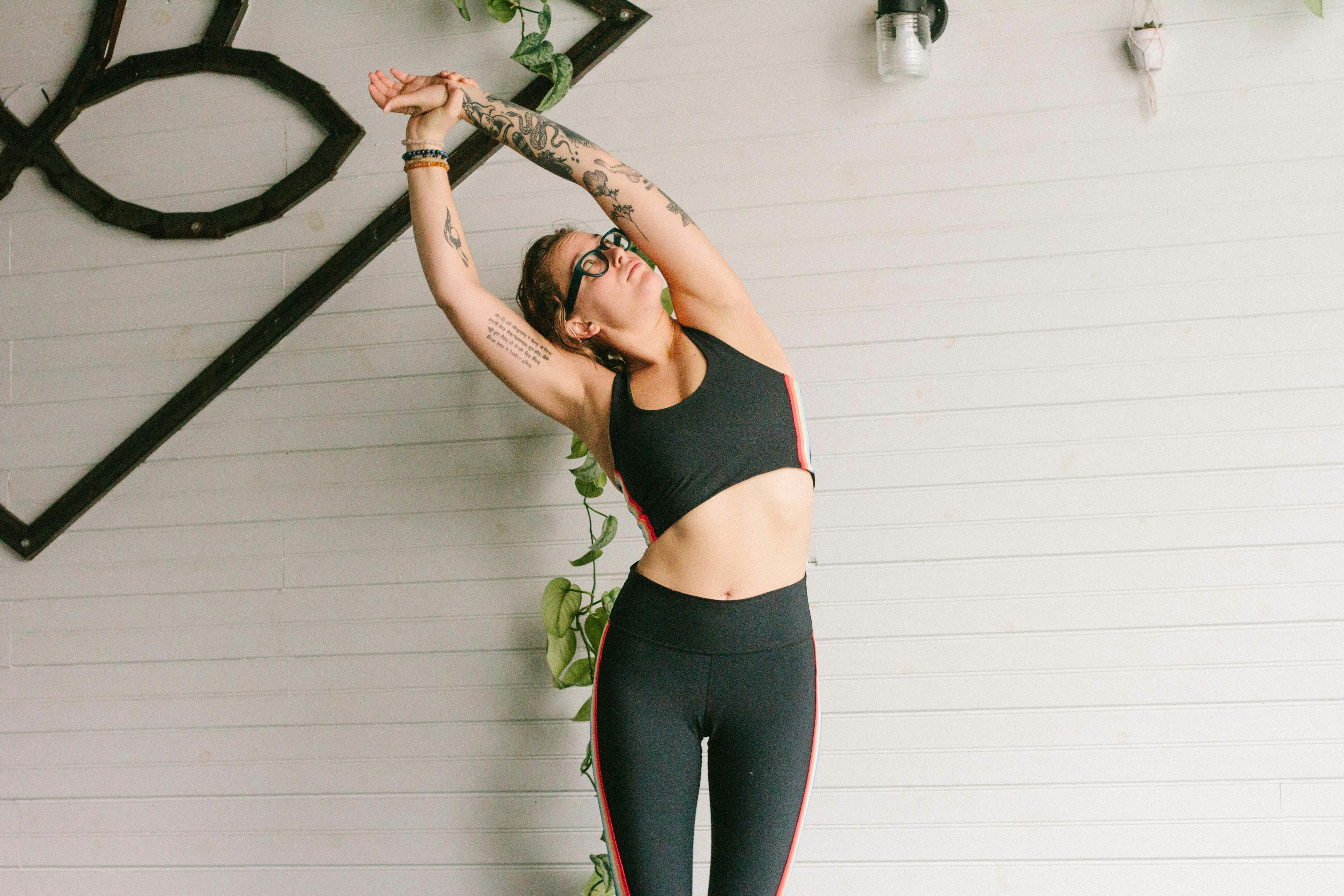 Woman in black performs the upward salute side bend yoga pose against a white wall back drop