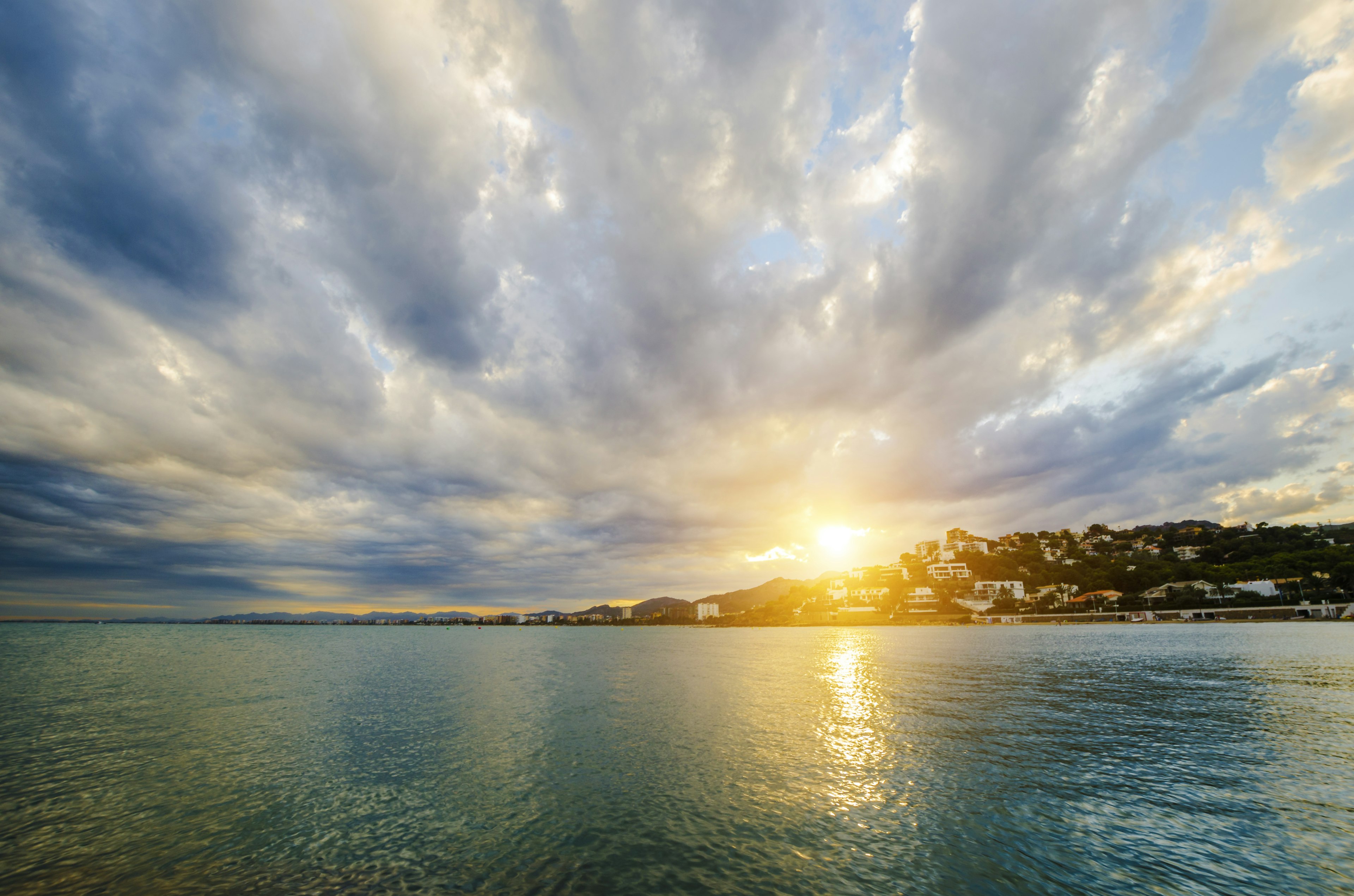 The sunsets behind a coastal European city with sparkling water in the foreground