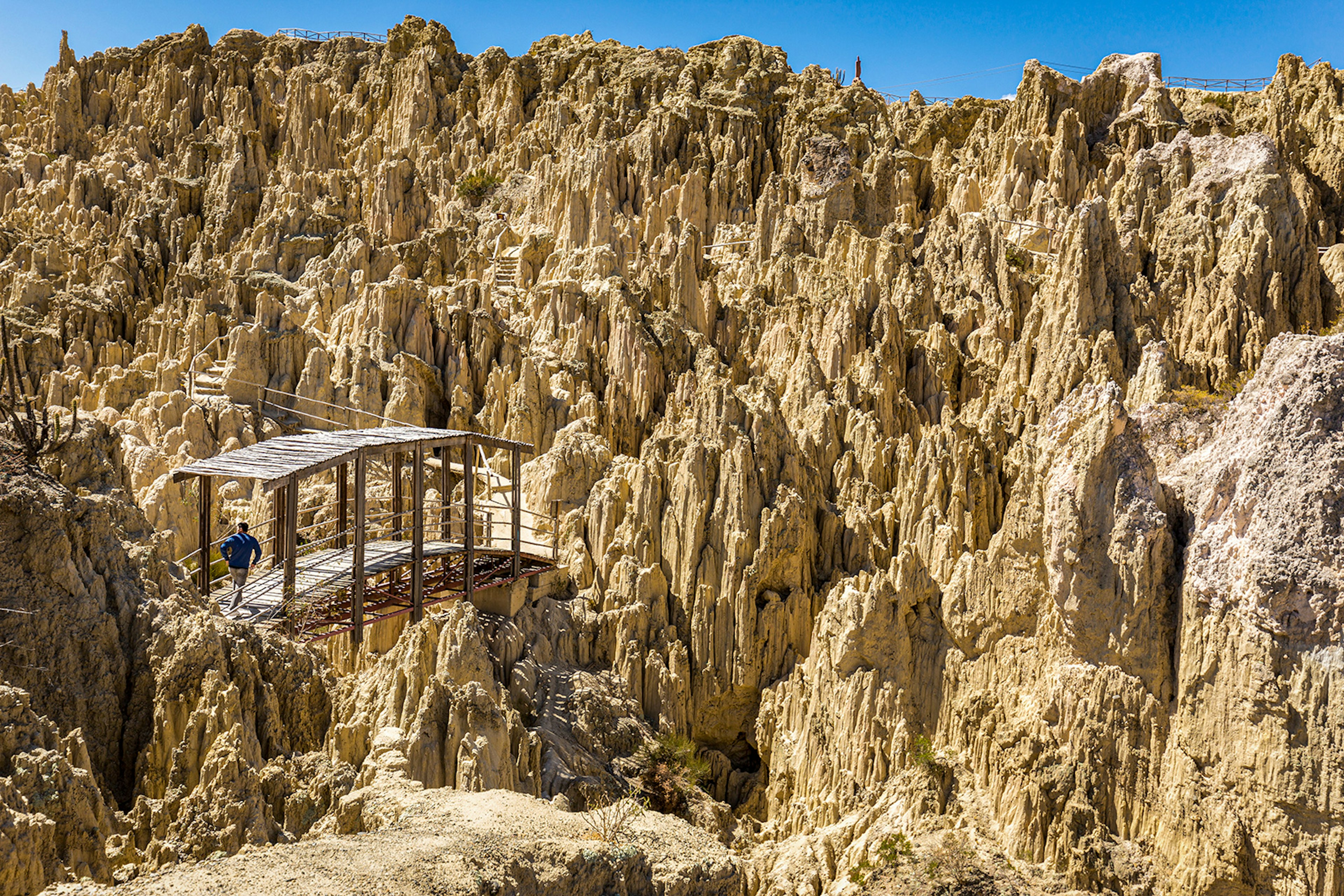 A person crosses a wood bridge among jagged geological formations in Valle de la Luna. La Paz, Bolivia.