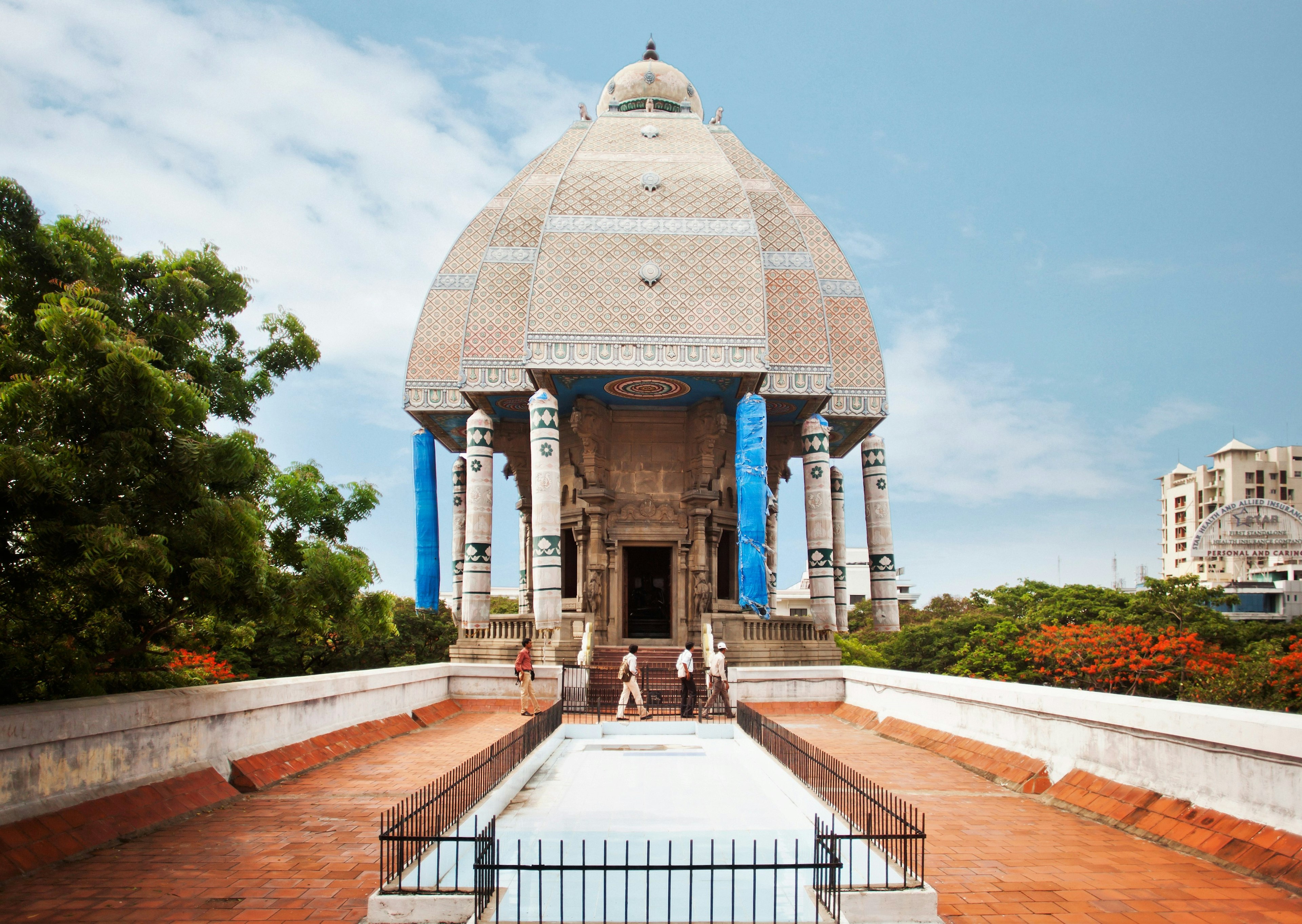 Three men walk past the entrance to the Valluvar Kottam: a large stone monument shaped like a temple chariot and dedicated to Tamil poet Thiruvalluvar