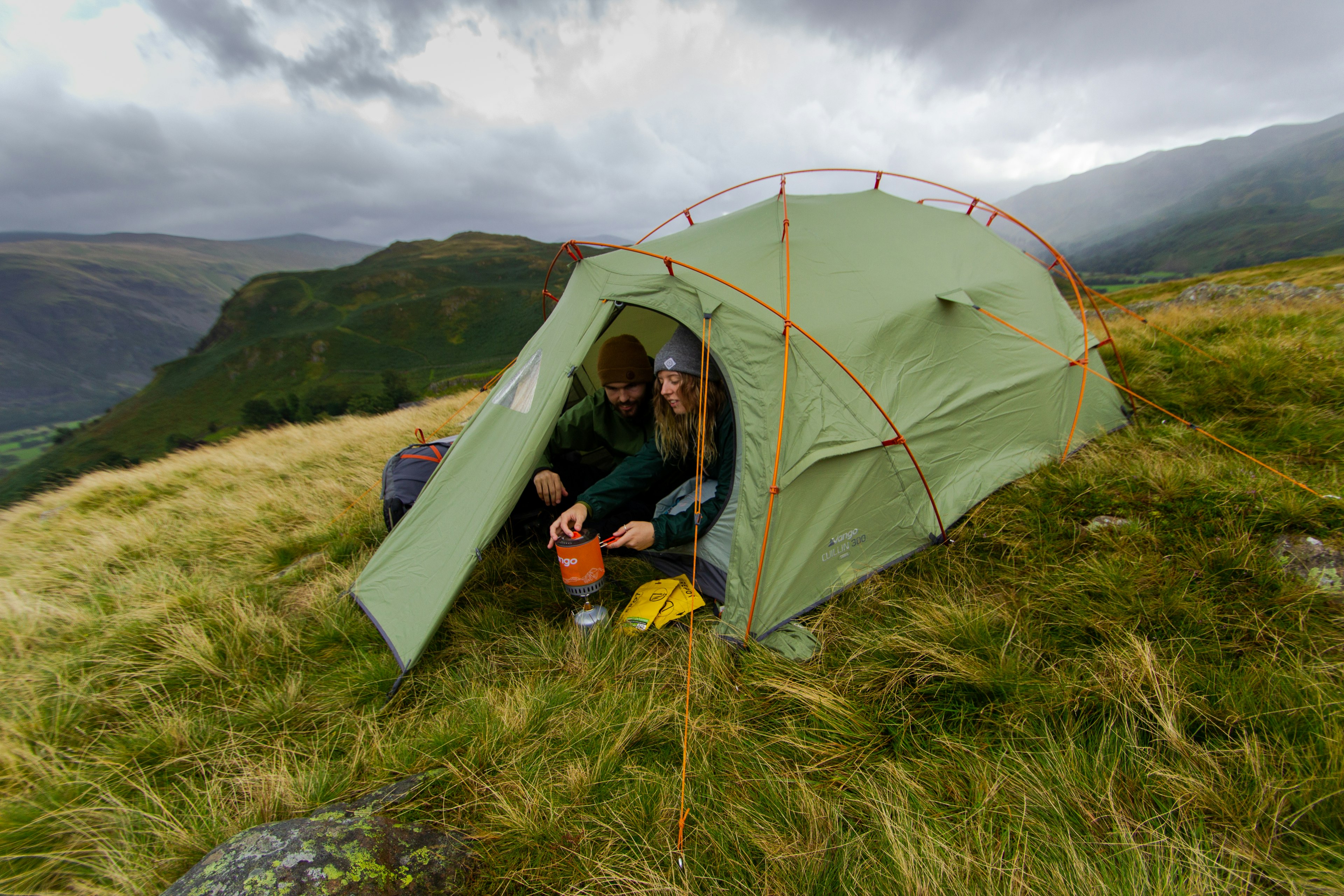 A man and woman use a stove from inside a tent