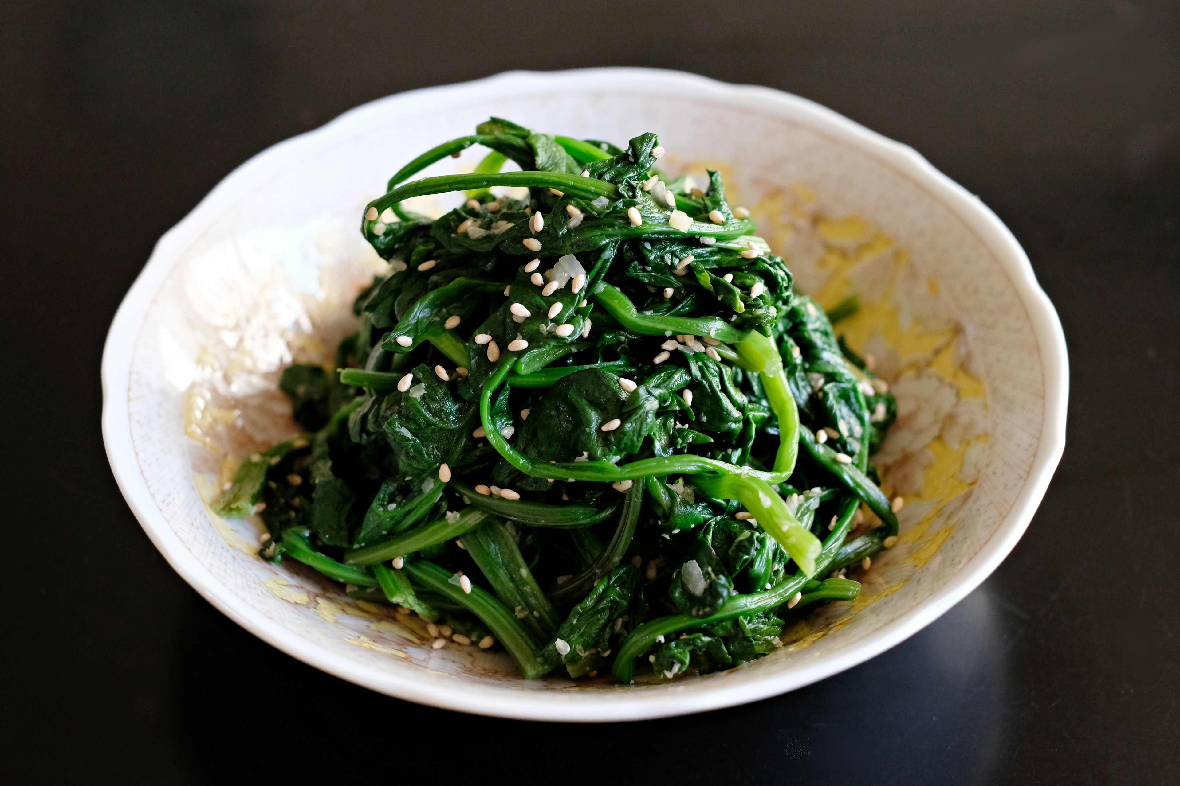 A mound of boiled and season spinach sits in a white bowl.