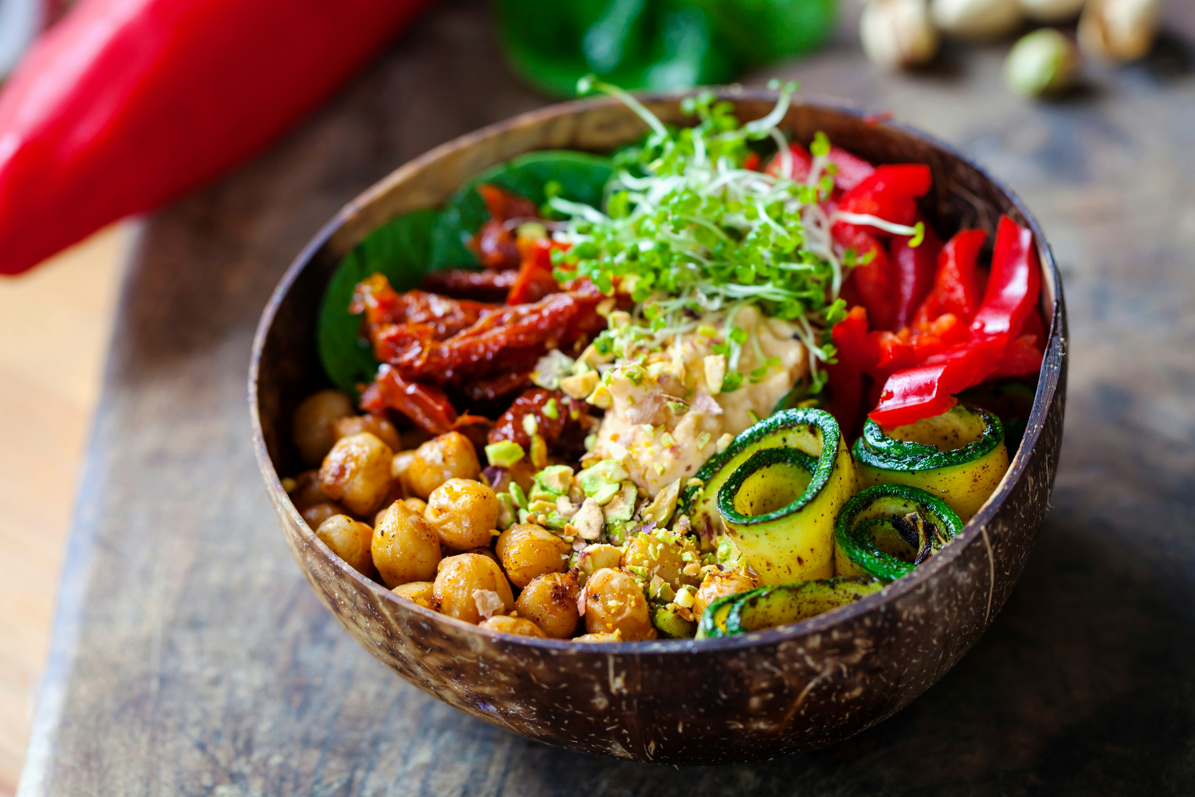 Closeup of a bowl filled with chickpeas, cucumbers, red peppers, sun-dried tomatoes and grains;