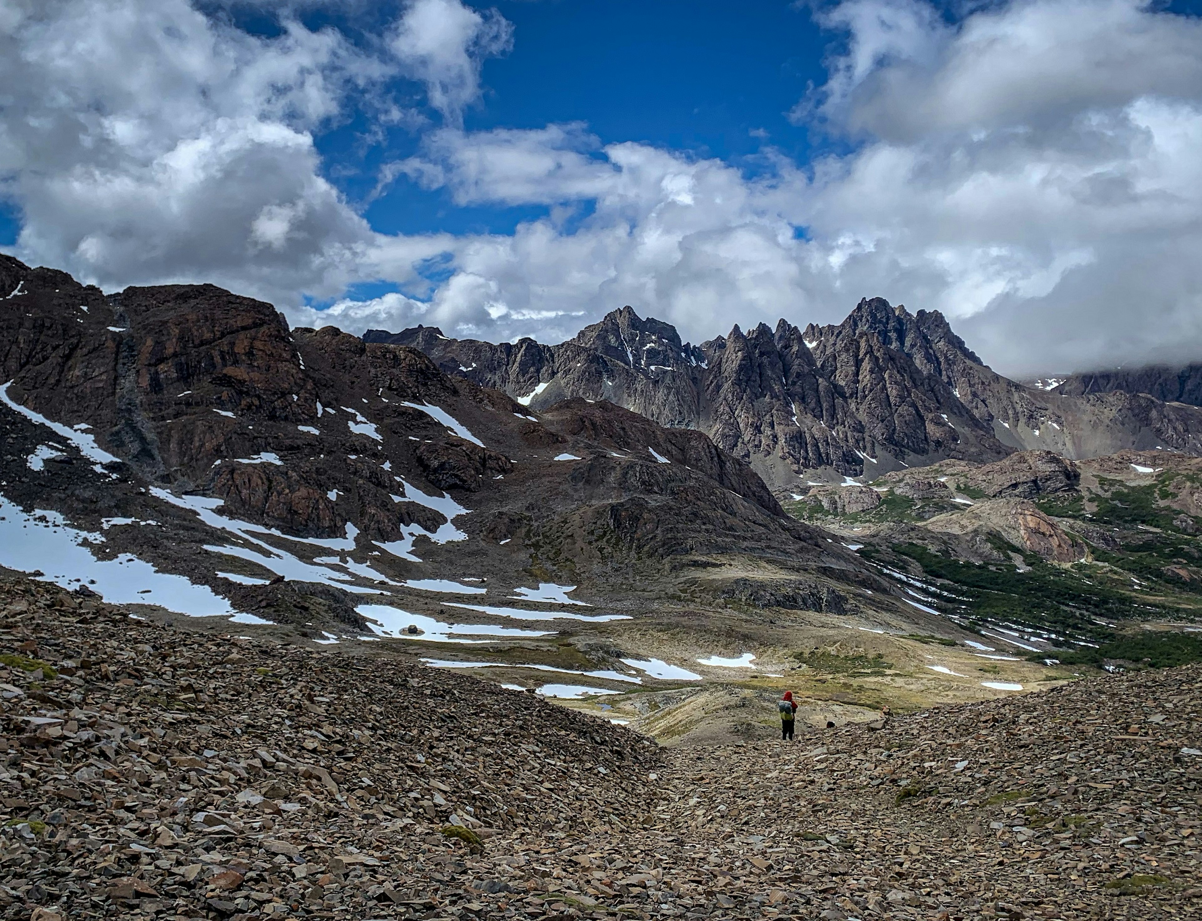 A single trekker stands in the distance with a mountain range stretching out ahead of them