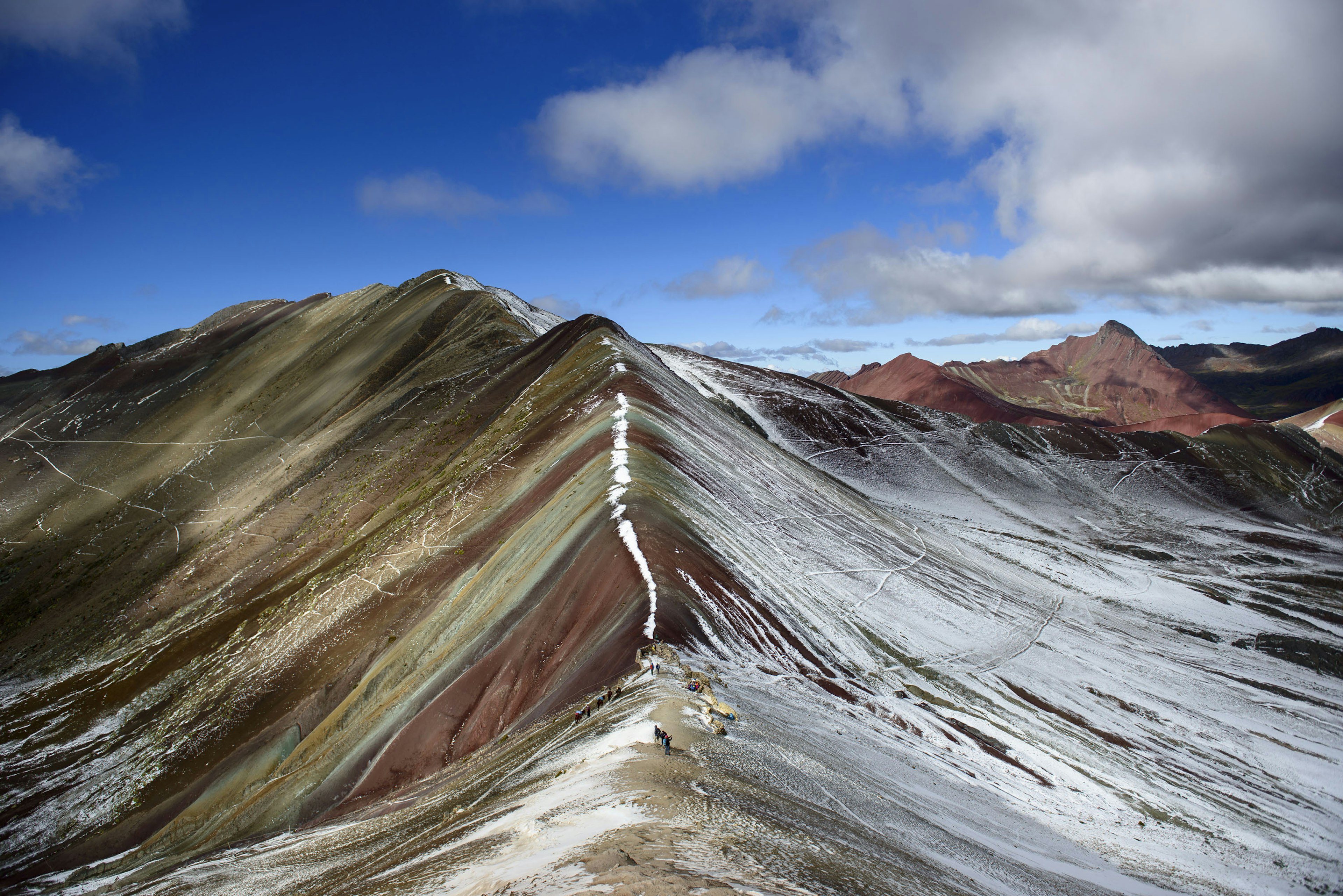 Snow slowly melts away to reveal the multi-color terrain of the Rainbow Mountains in Peru