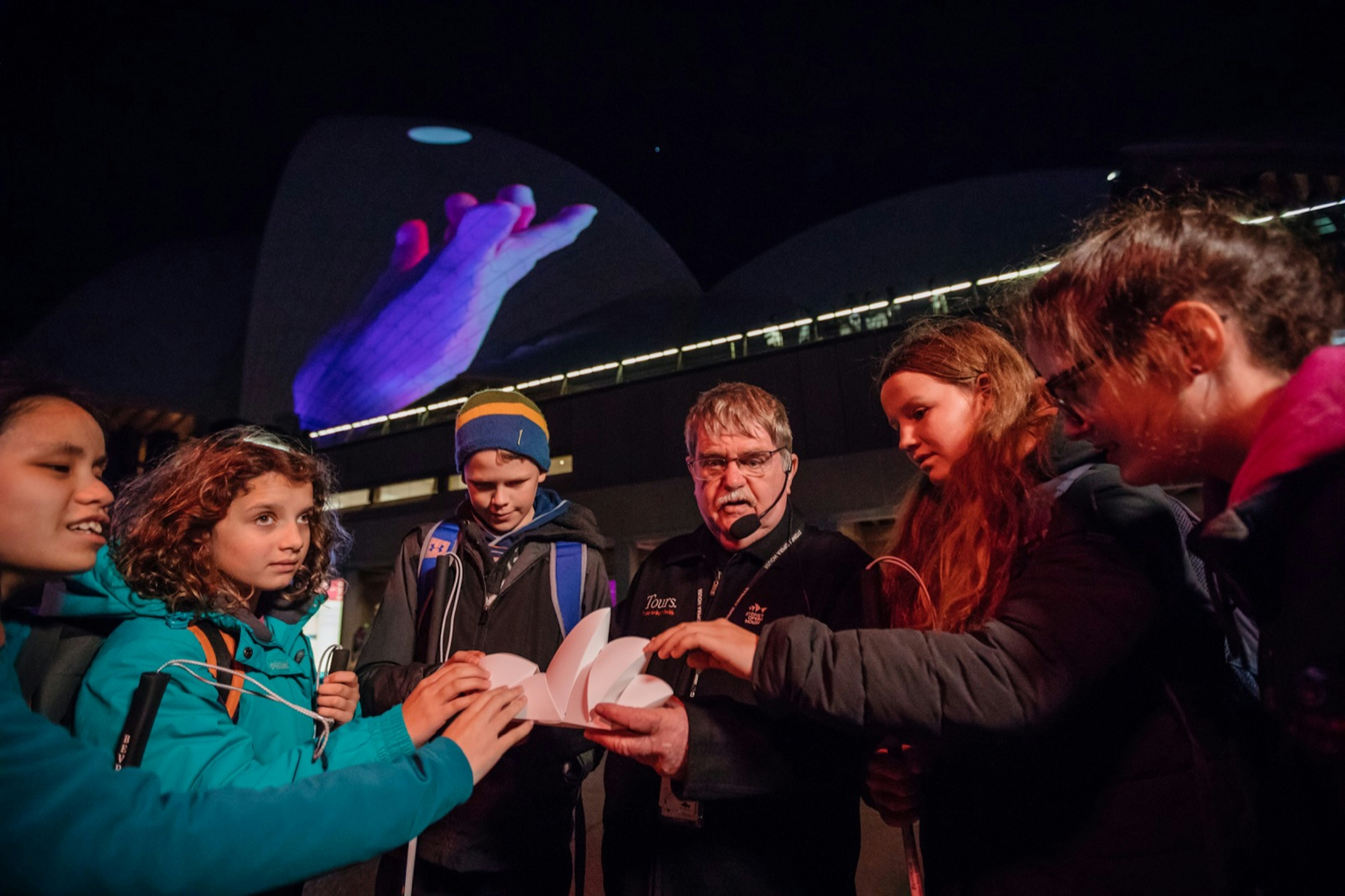 a group of kids touches a model of the Sydney Opera House as a man talks into a microphone; accessible Australia