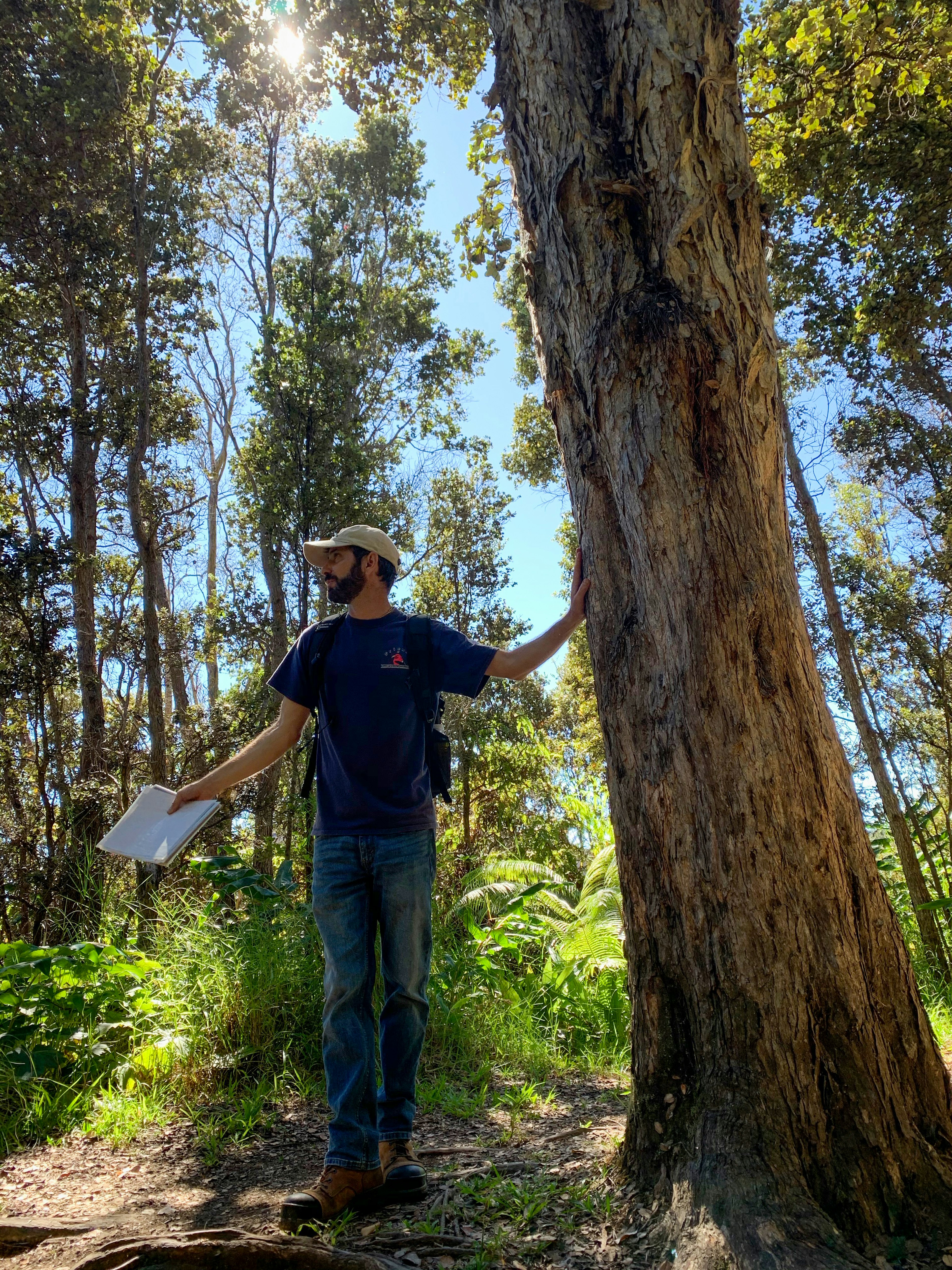 A Friends of Hawai'i Volcanoes National Park guide stands next to a tree, holding a book.