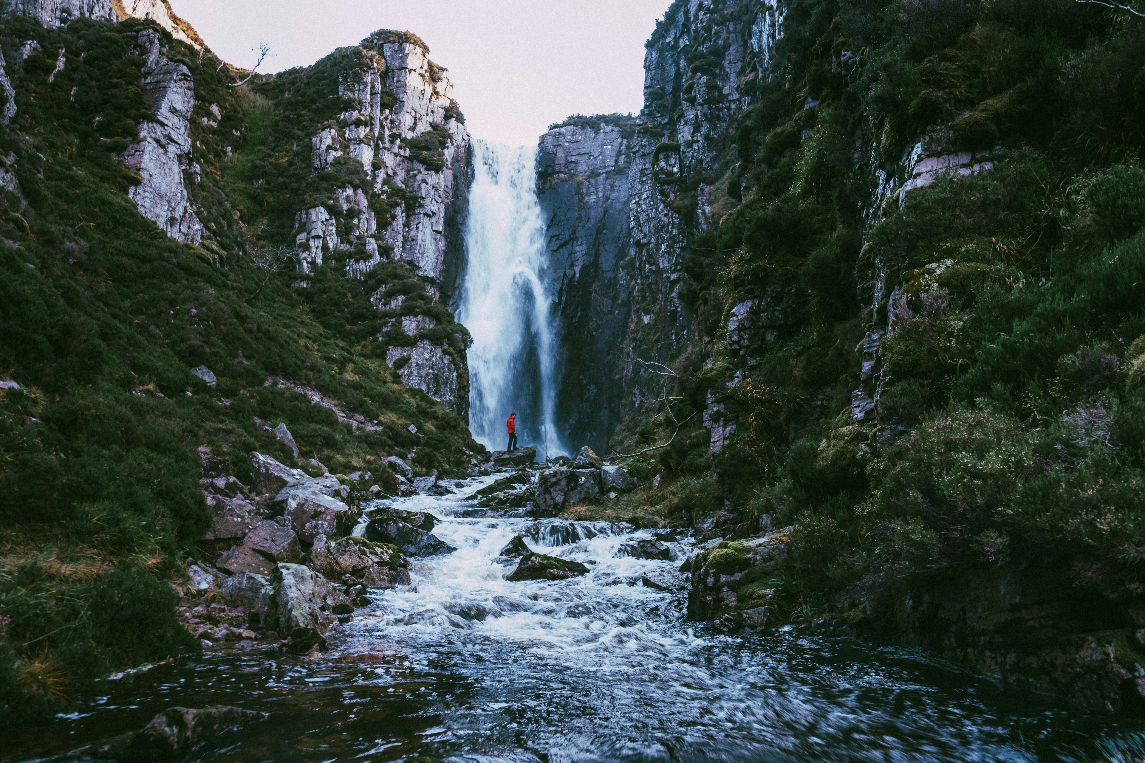 A man in a red jacket stands at the foot of the Wailing Widow Waterfall.