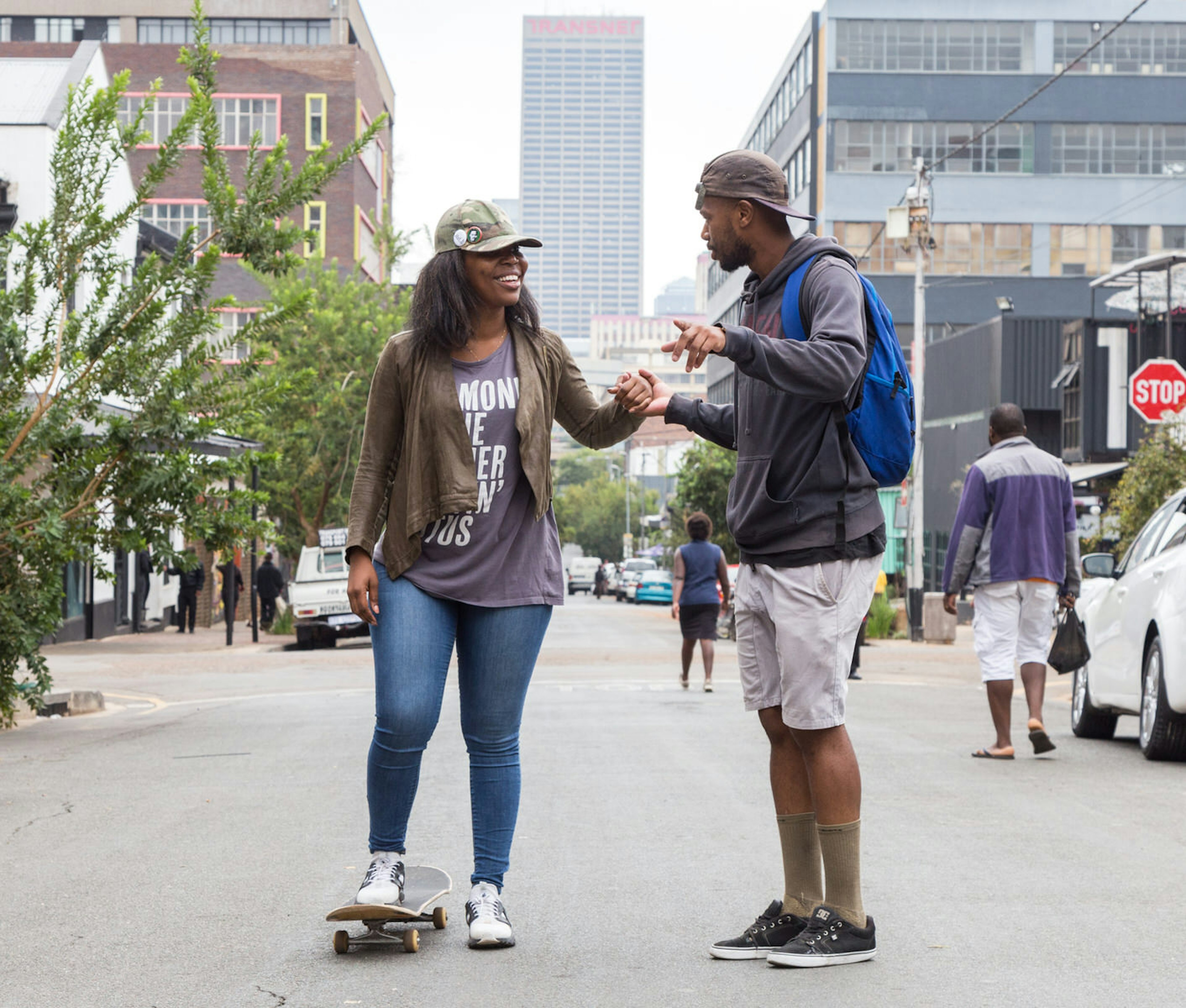 A smiling woman stands on a skateboard with one foot while her guide holds her hand and offers direction © Heather Mason / ϰϲʿ¼