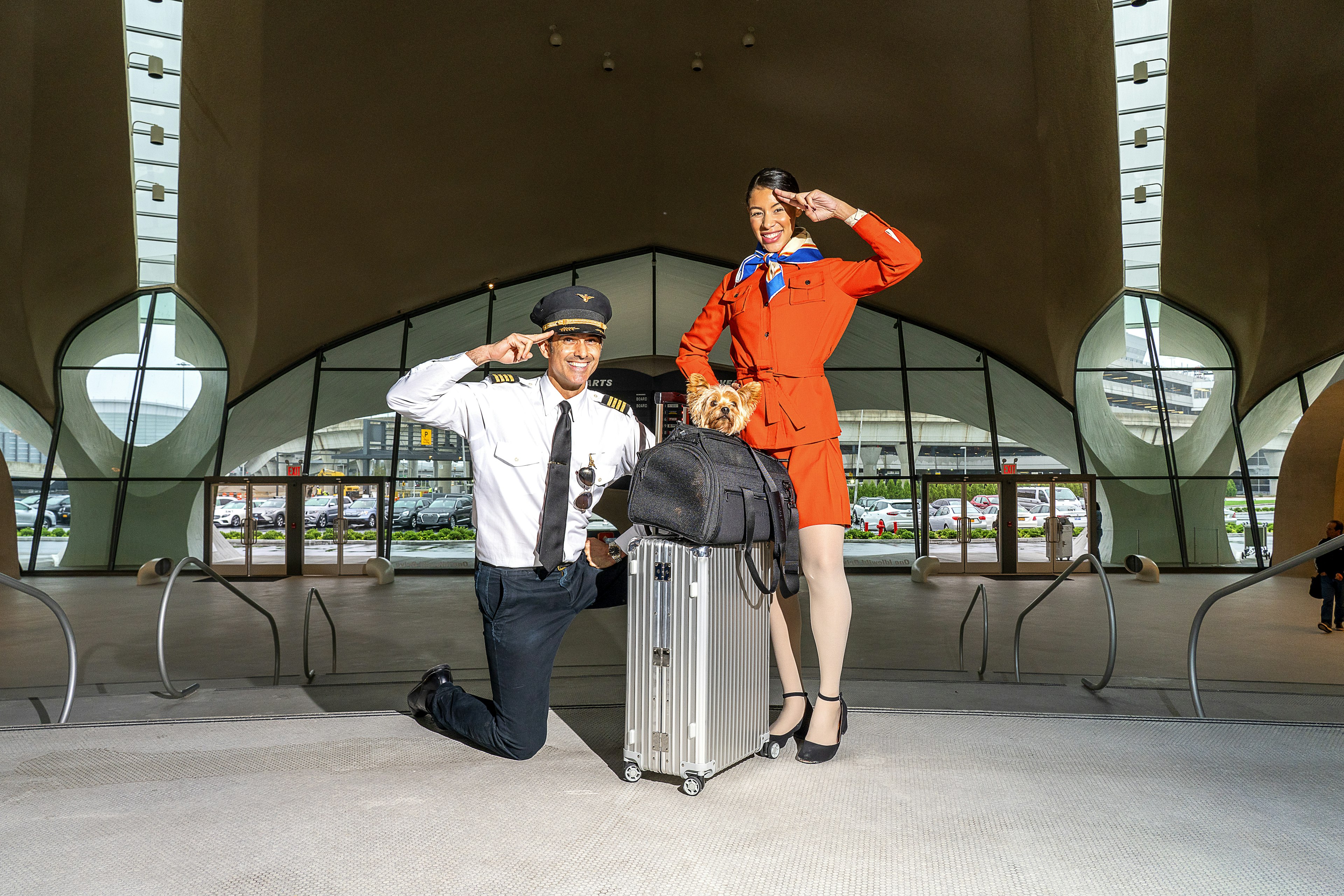 A pilot and a flight attendant standing by suitcase topped with a small dog in a Wild One Air Travel Carrier