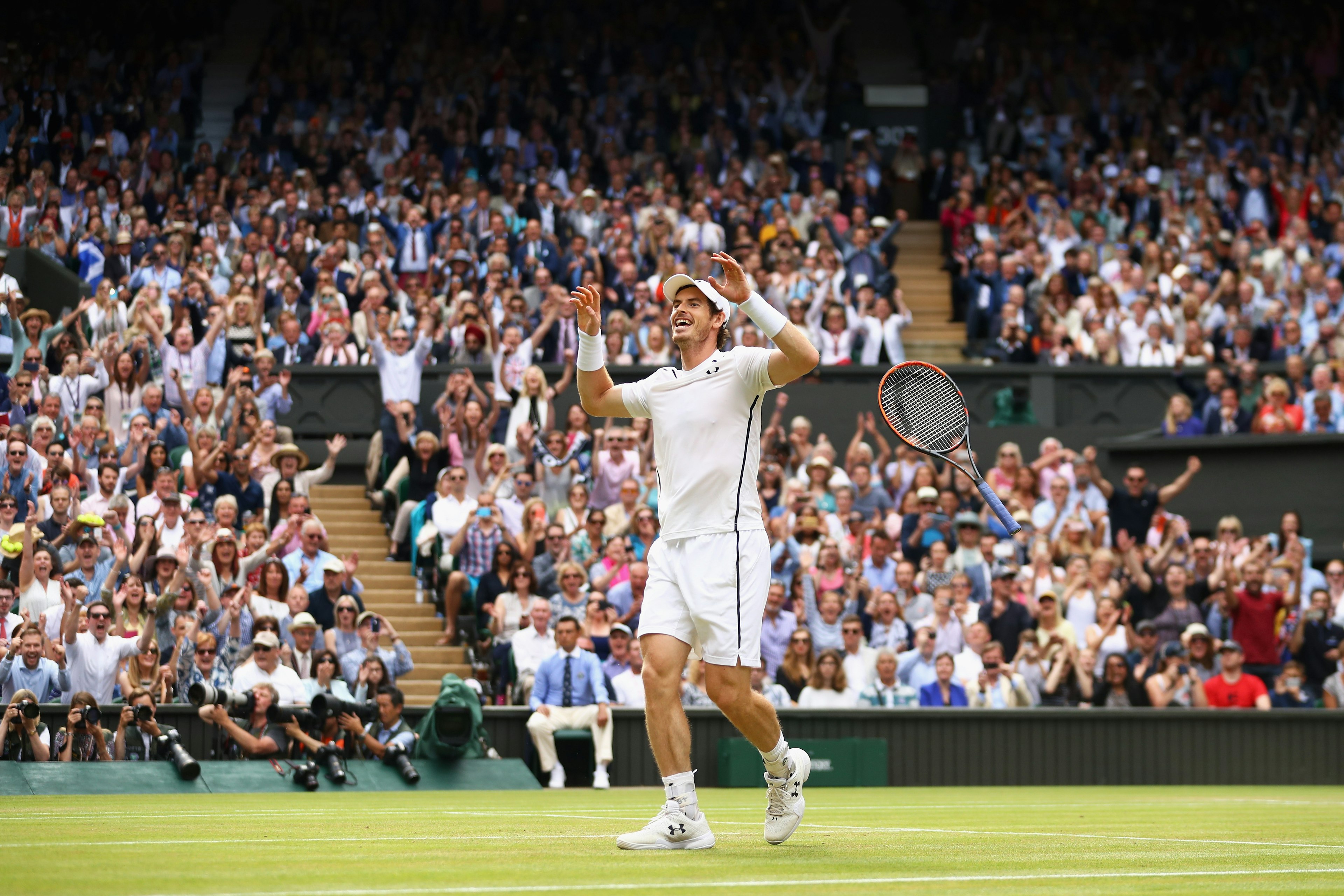 Tennis player Andy Murray celebrates at Centre Court during a Wimbledon Final. Rows of fans cheer in the background.