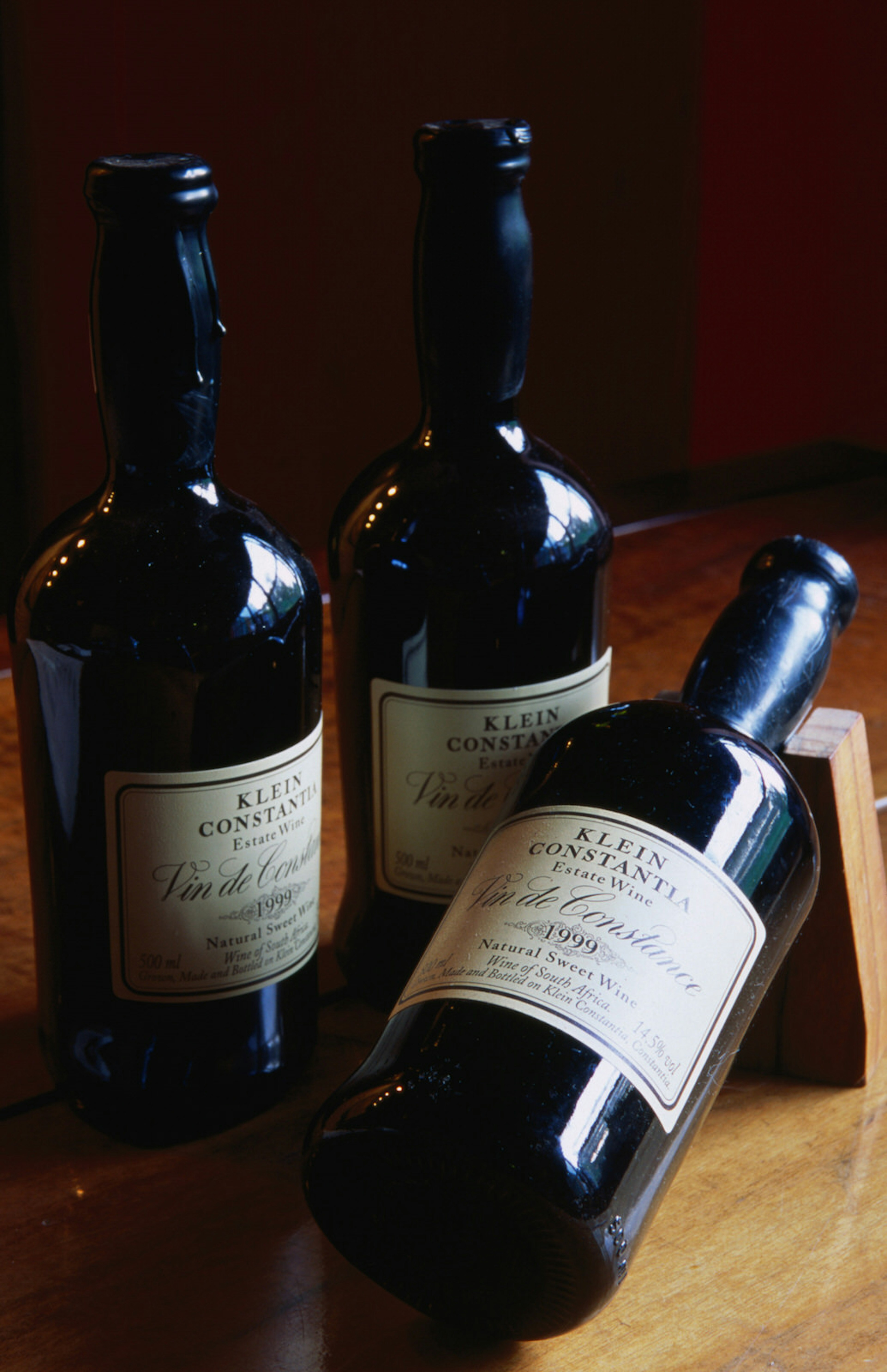 Three bottles of red wine, two standing and one laying horizontally, sit in a low wooden box on a table