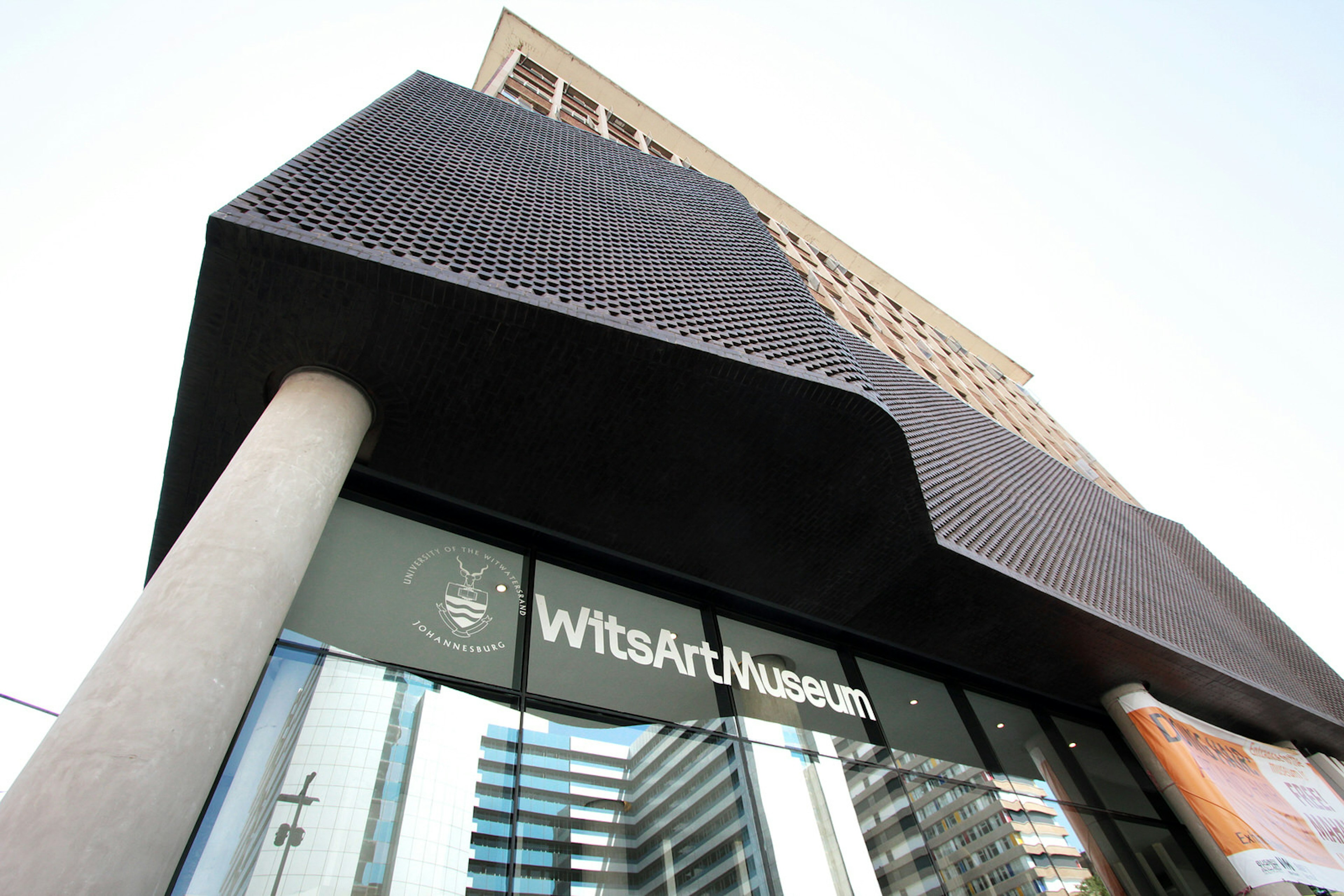 Johannesburg June - Shot from the street looking upwards to a large modern tower block of pinkish stone, with its 1st floor clad in sculpted black metal; the ground floor is encased in glass, with the sign for the Wits Art Musum emblazoned in white lettering