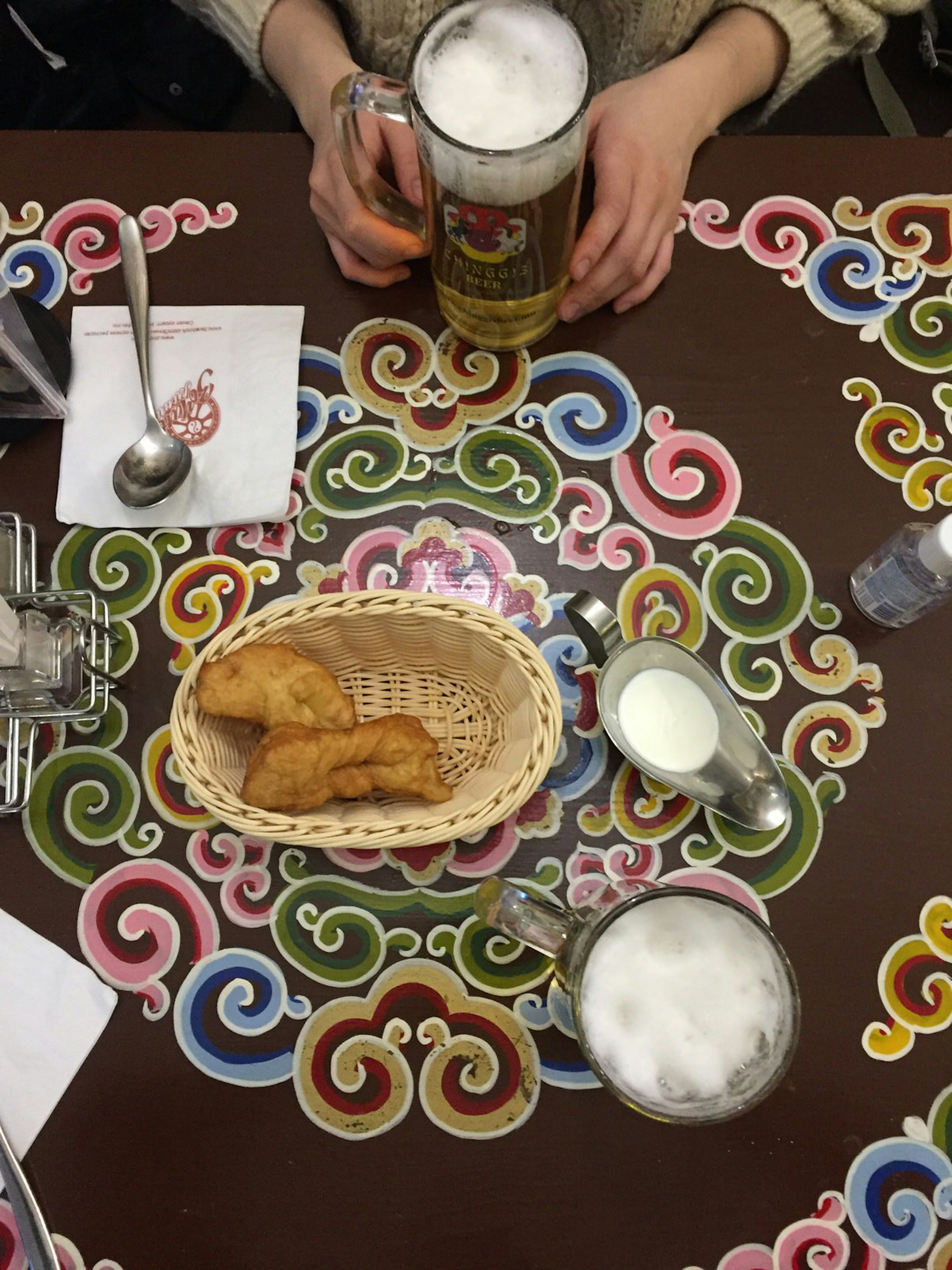 Top-down view of a table top, on which stands two beers and some fried bread in a wicker basket.