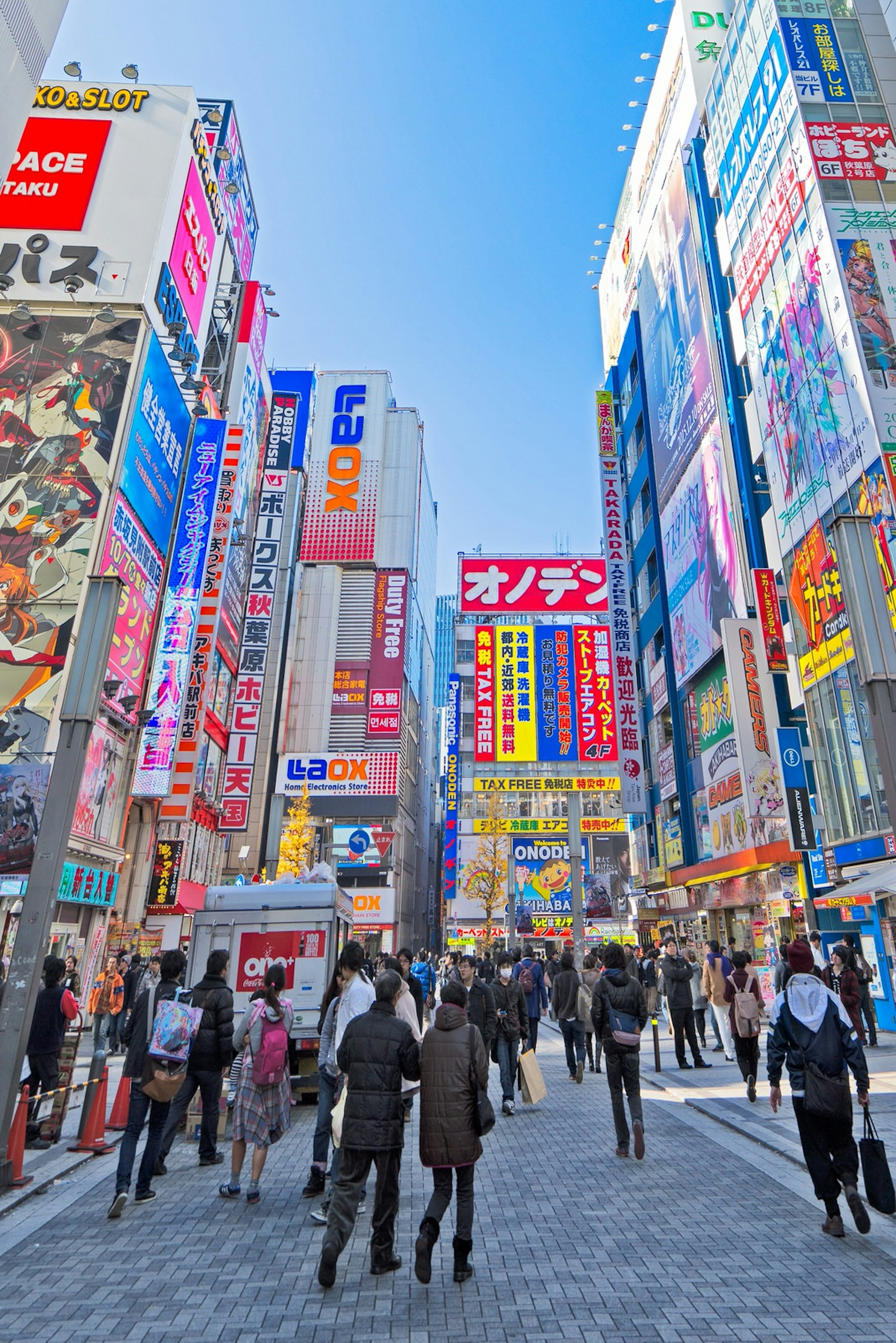 Shoppers walk along a narrow street in Akihabara, tall buildings covered with bright signs on either side © easy camera / Shutterstock