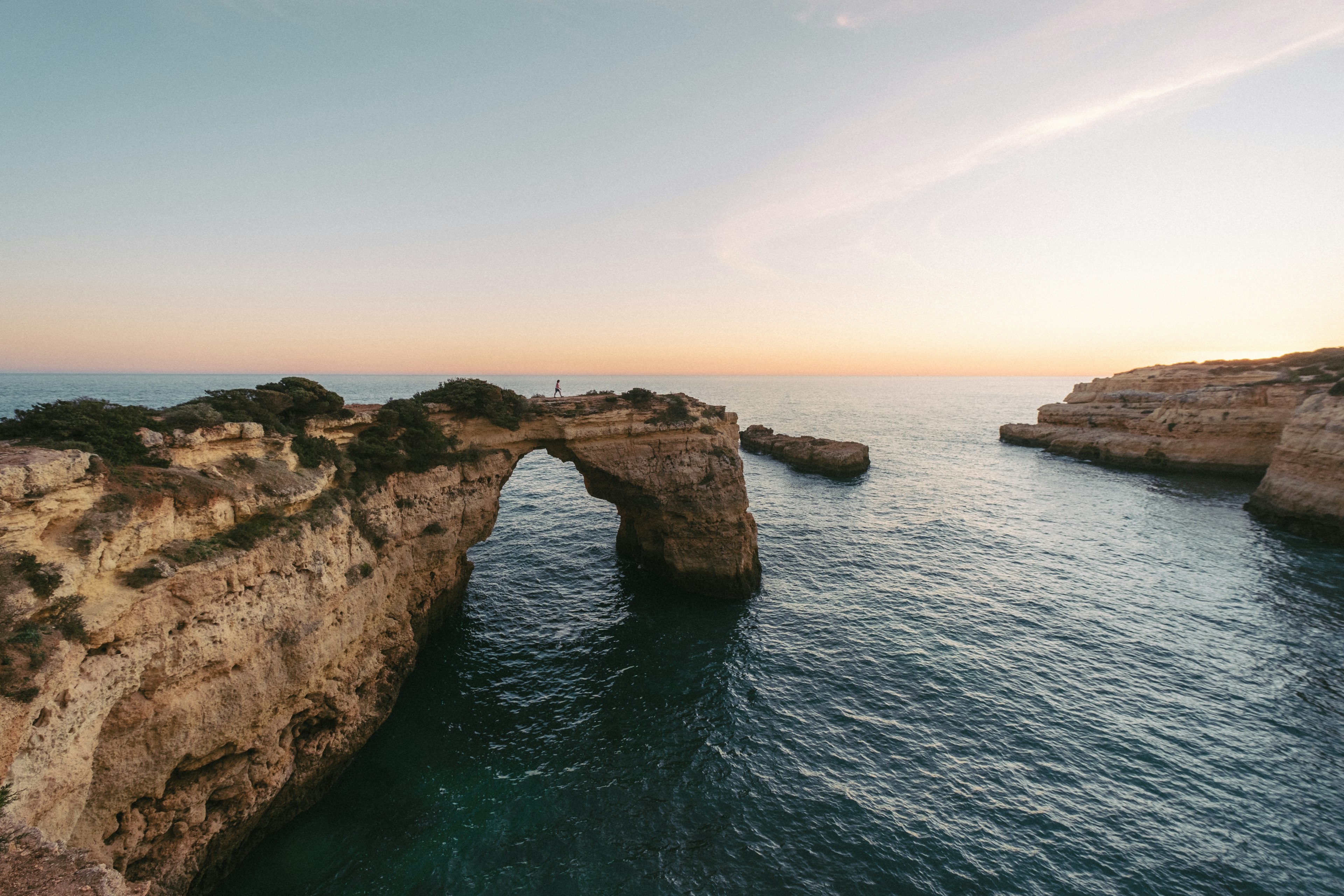 Coastal rock has been eroded to form the prominent Albandeira Arch; a lilac-hued sky at dawn rests above.