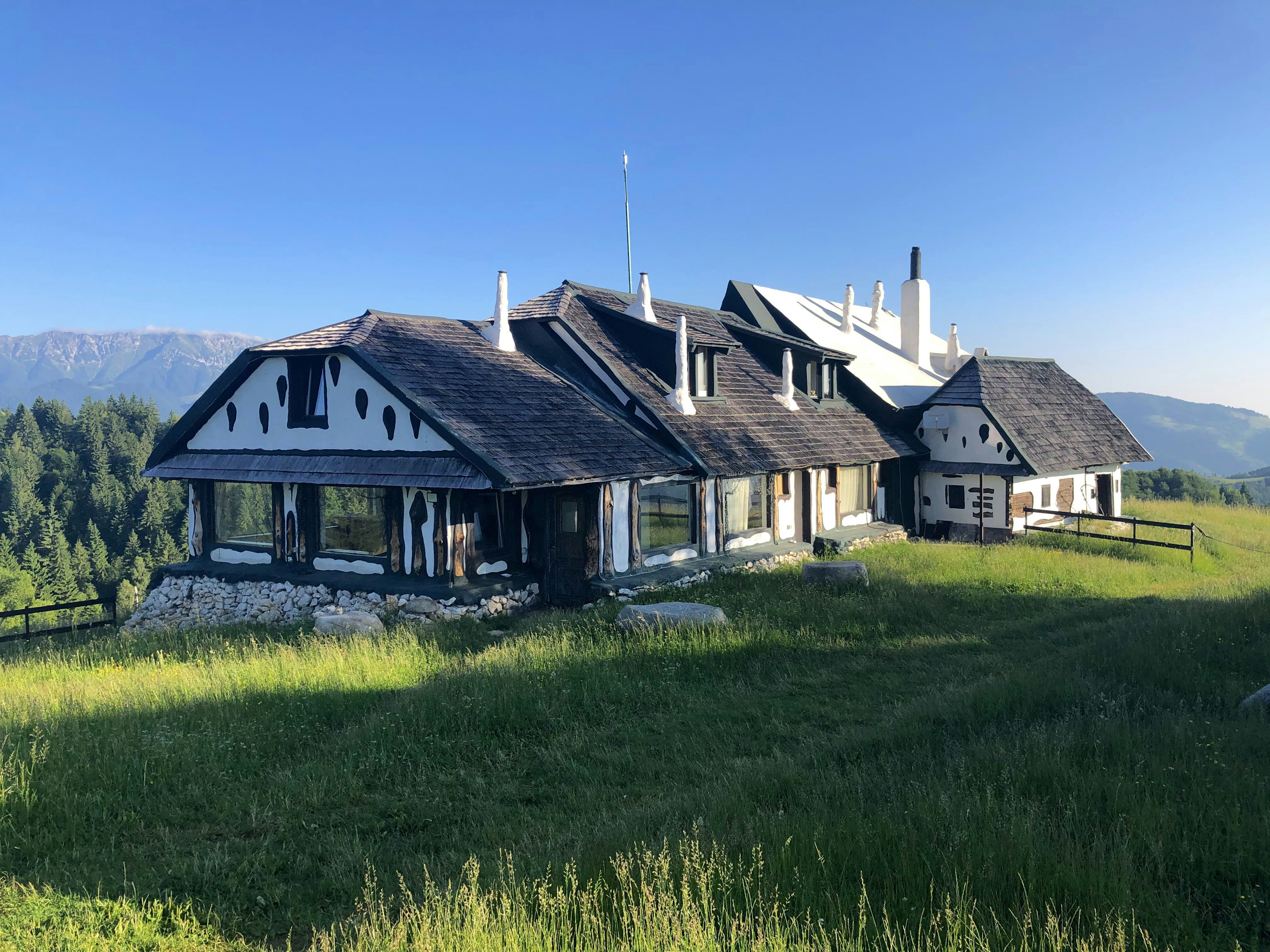 A quirky, but rather large fairy-tale-like cabin with wood-shingled roof sitting in a grassy field.