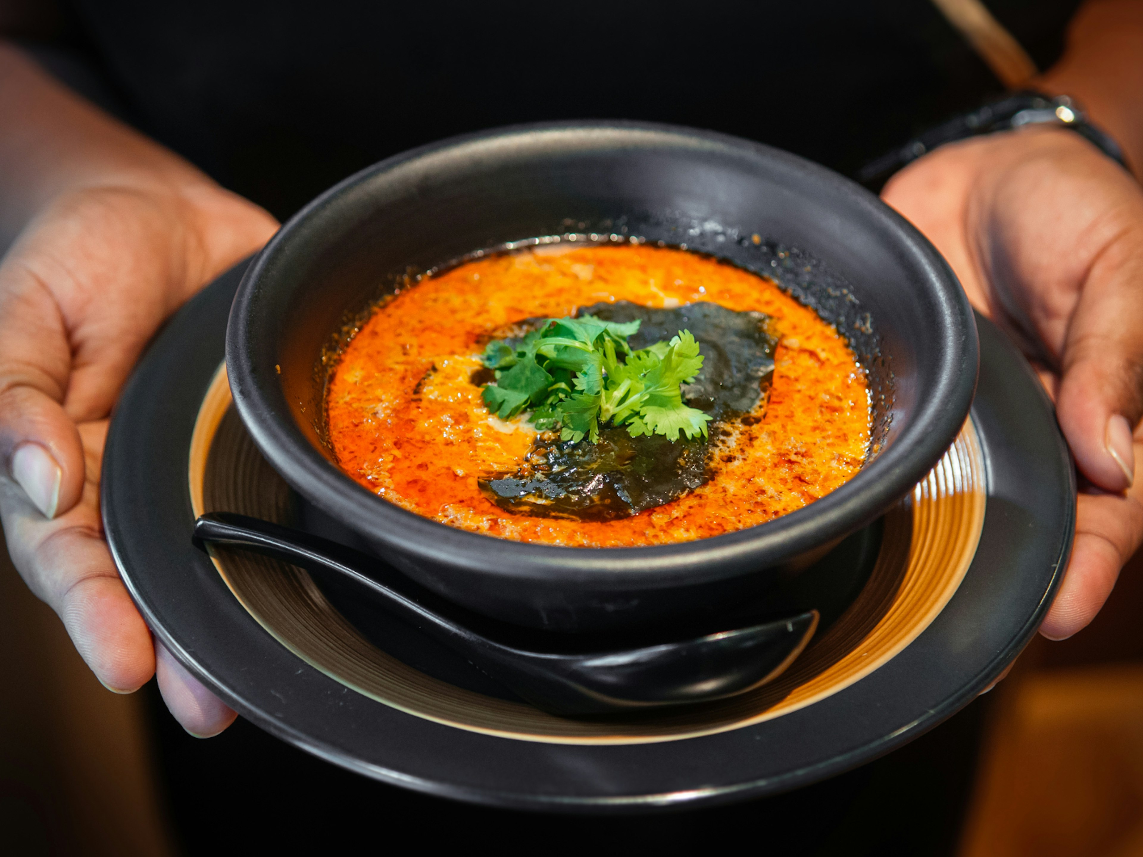 Waiter holds Peranakan dish ayam buah keluak (nut chicken stew curry) in a bowl