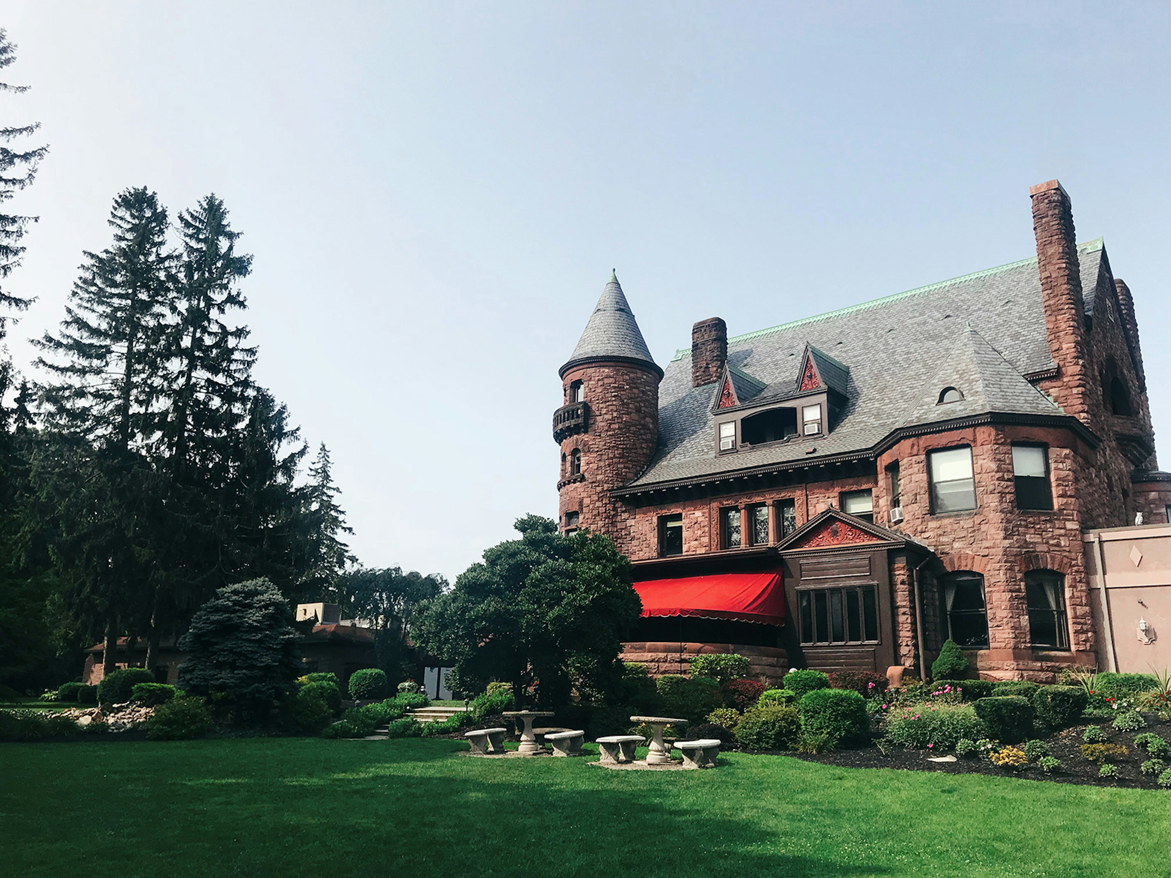 Exterior shot of brownstone castle-like mansion, Belhurst Castle, in the Finger Lakes against a blue sky with green grass and tall pine trees © Mikki Brammer / Lonely Planet